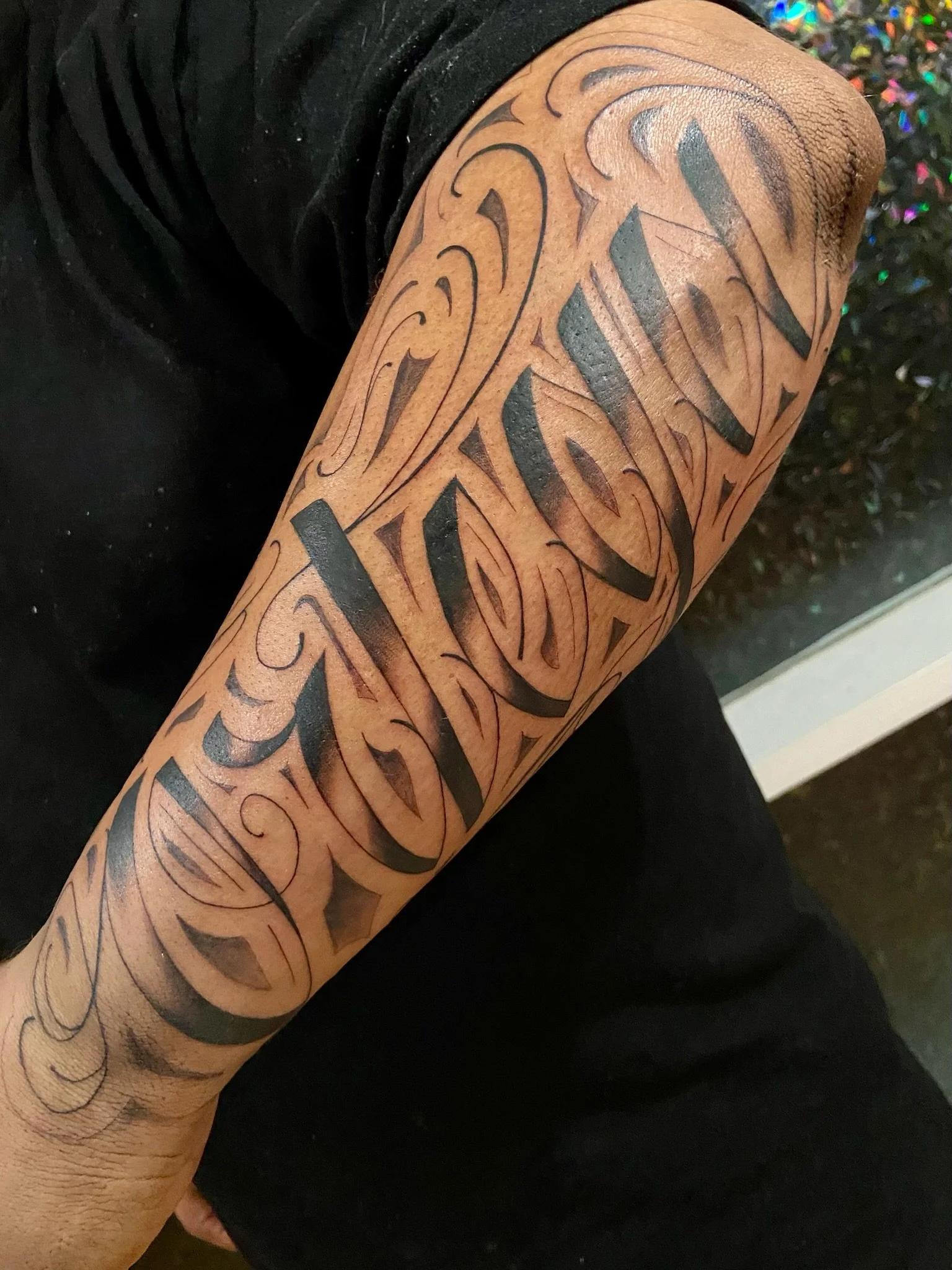 Close-up of a person's arm with a tattoo featuring intricate black abstract and tribal designs.