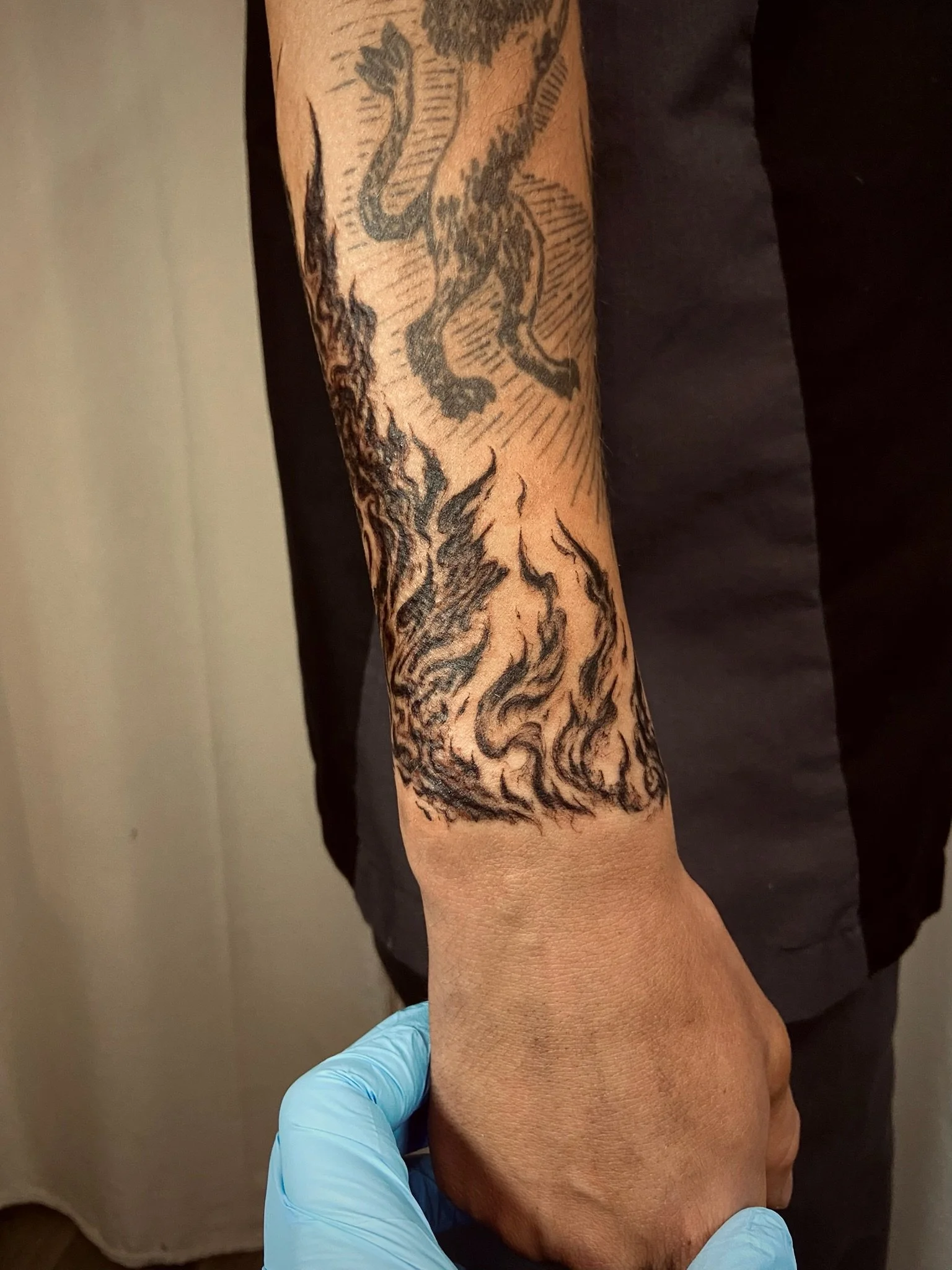 A person receiving a tattoo of a dragon on their forearm, with the tattoo artist wearing gloves.
