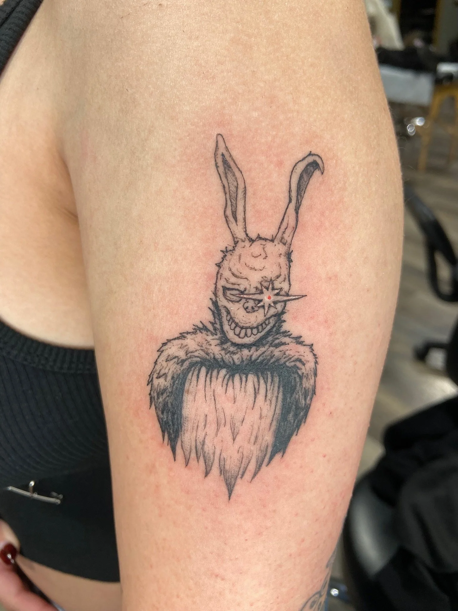 Tattoo of a rabbit with a mischievous expression, holding a star-shaped object with a red dot in the center, on a person's upper arm.
