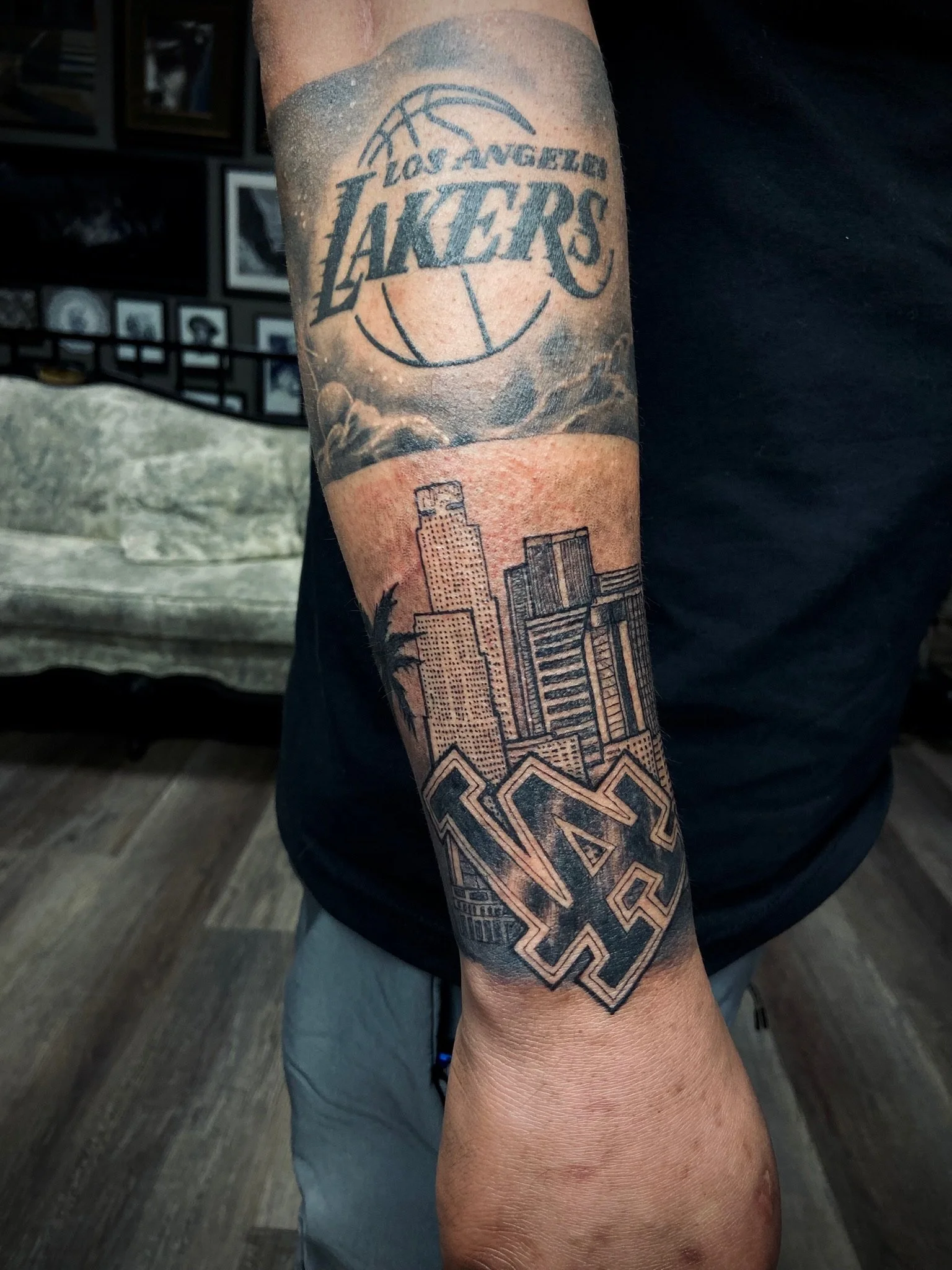 Tattoo on person's arm featuring the Los Angeles Lakers logo and city skyline.