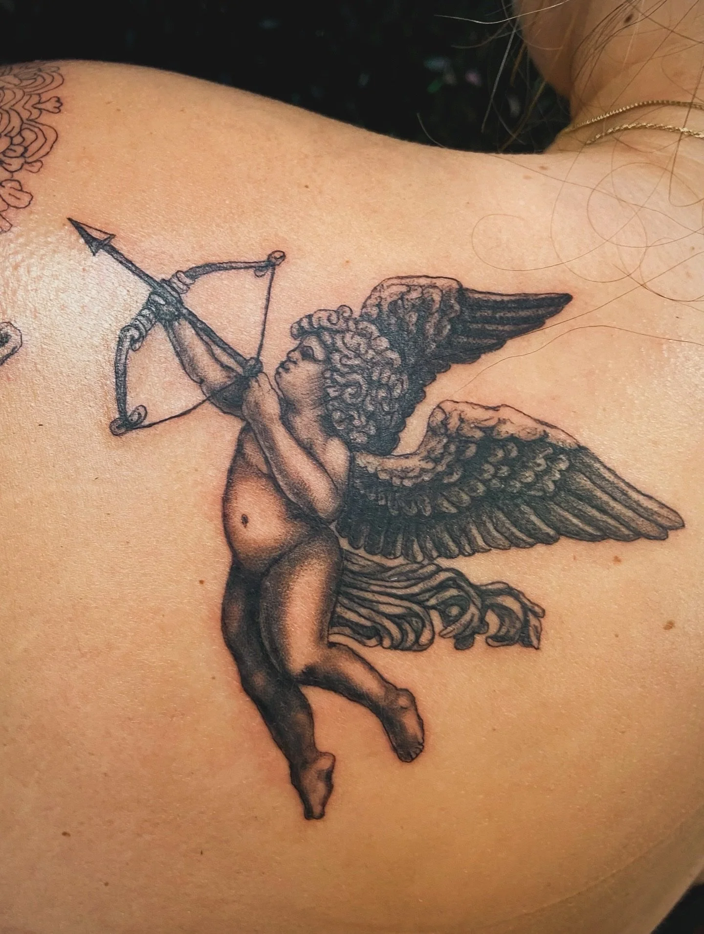 Tattoo of a Cupid figure with wings, holding a bow and arrow, on a person's skin.