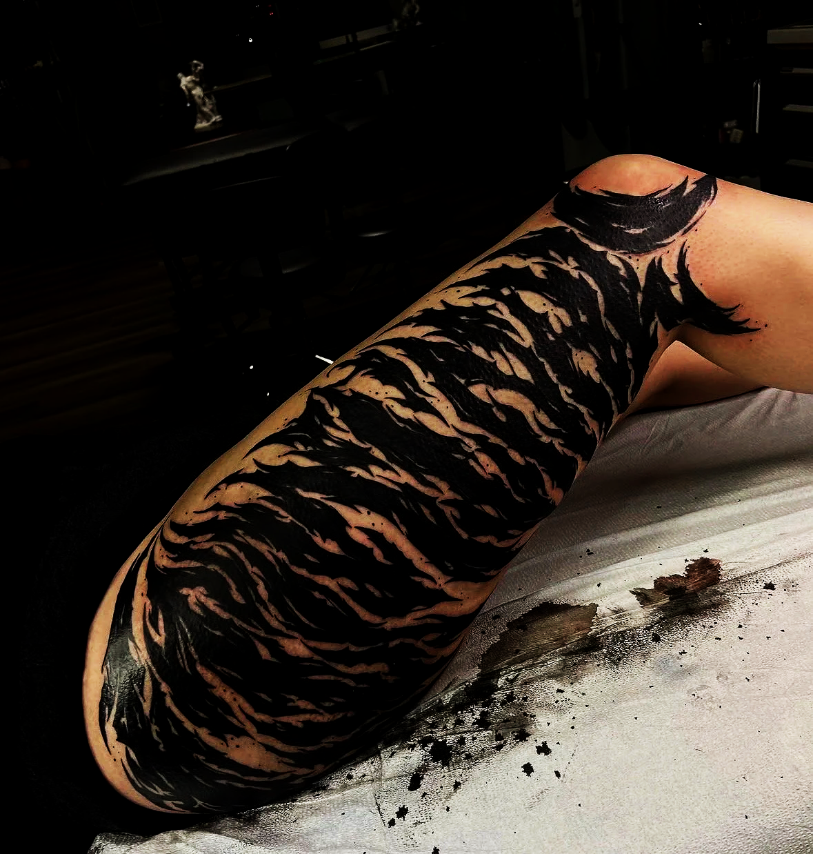 Close-up of a woman's leg with black abstract blackwork tattoo art extending from the thigh to the ankle, lying on a surface with ink splatters by tattoo artist Agua at Floating Streams Tattoo in the Arts District of Downtown Los Angeles.