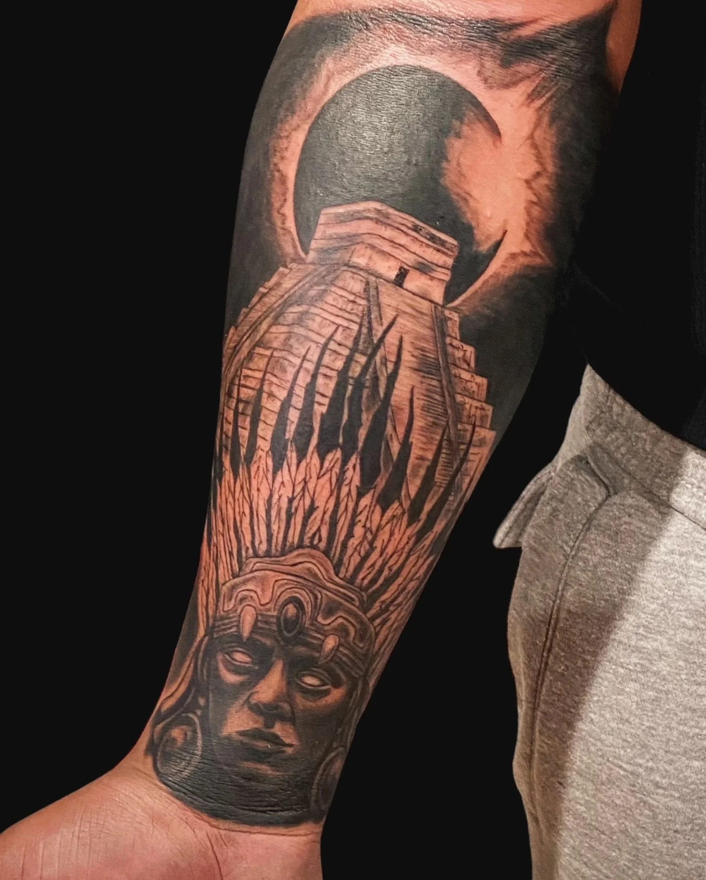 Tattoo of a woman with a headdress, an ocean scene with a lighthouse, and a sunrise or sunset on the arm.