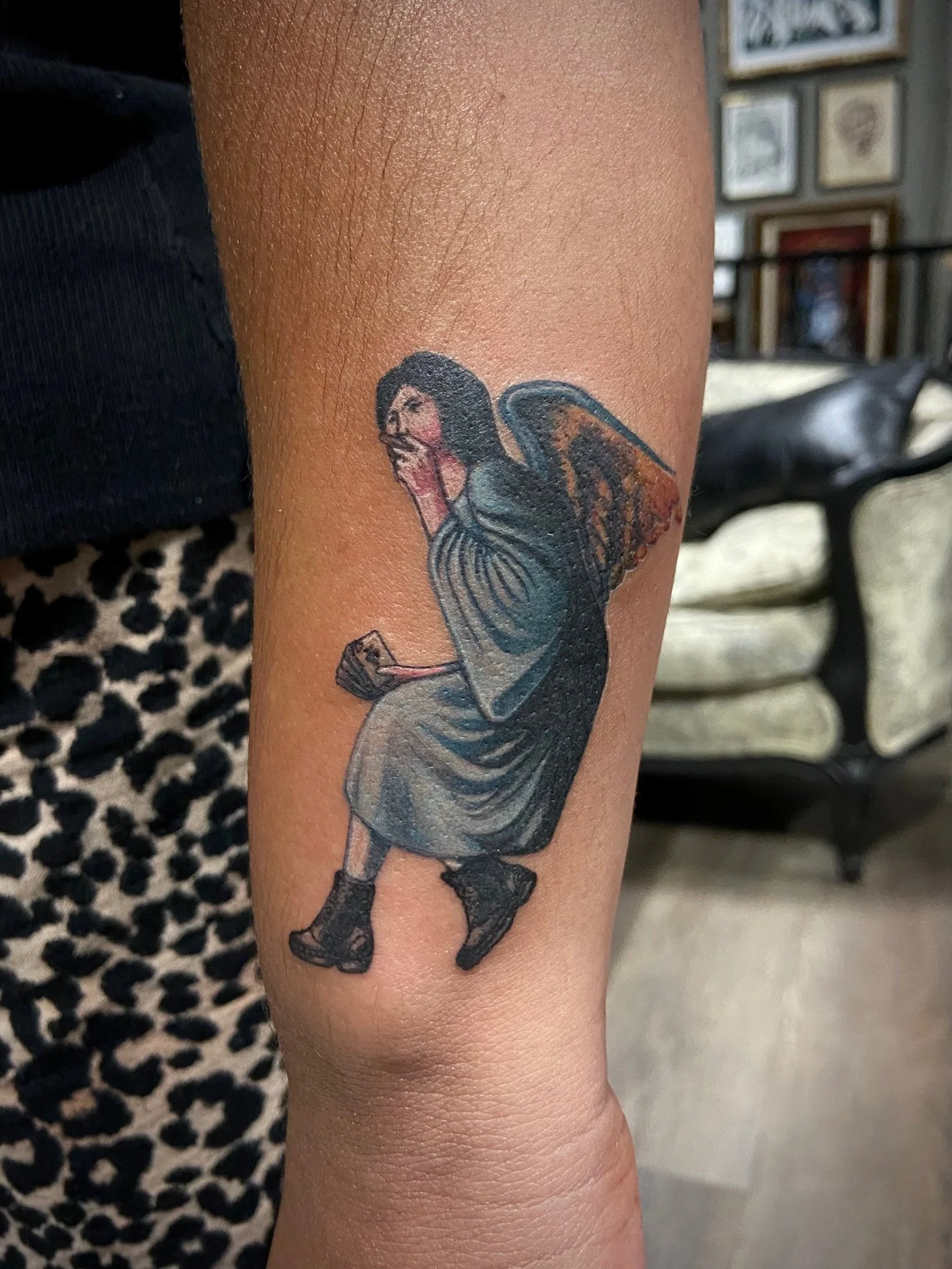A tattoo of a woman with dark hair, dressed in gray clothes, with butterfly wings, appears on a person's arm.