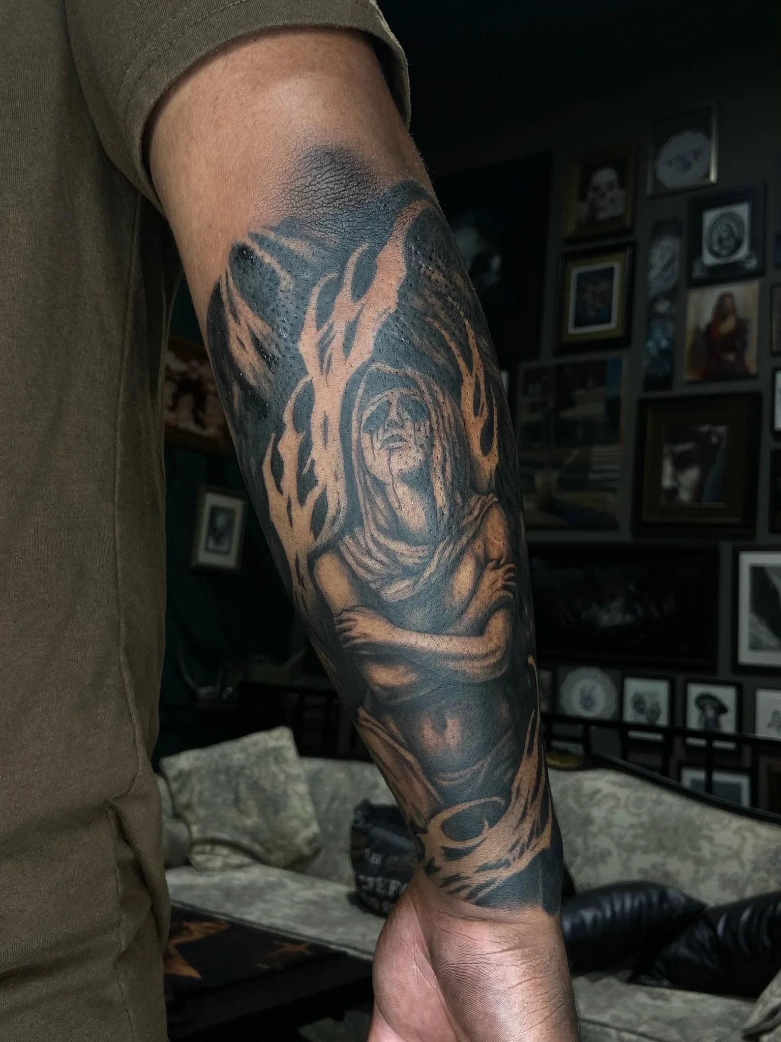 Close-up view of a person's arm with a detailed black and gray tattoo, depicting a woman with flowing hair and intricate background art.