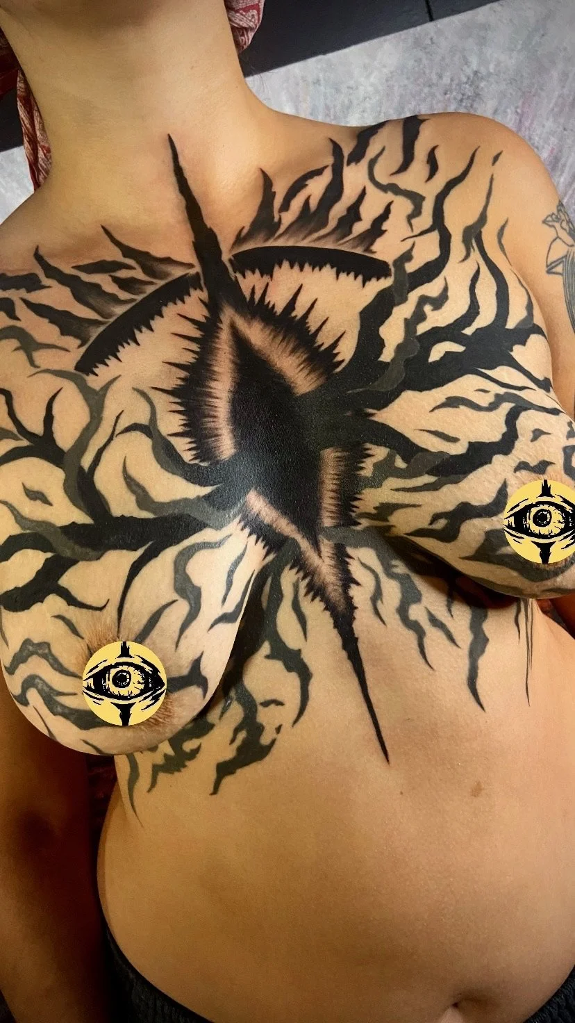 A person with a large black and white tattoo resembling a tree and a star on their chest and breasts.