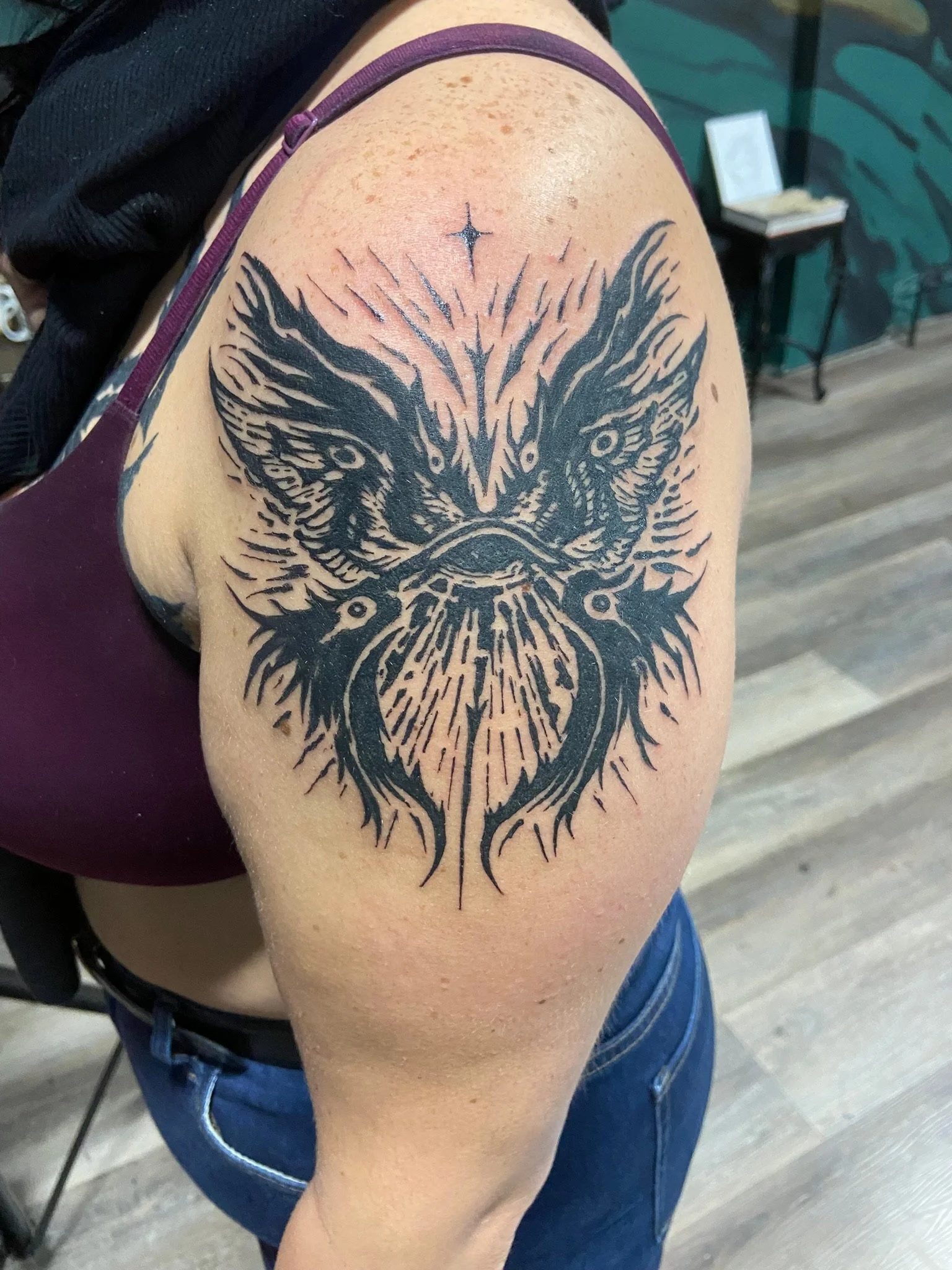 A tattoo of an owl with spread wings on a person's upper arm.