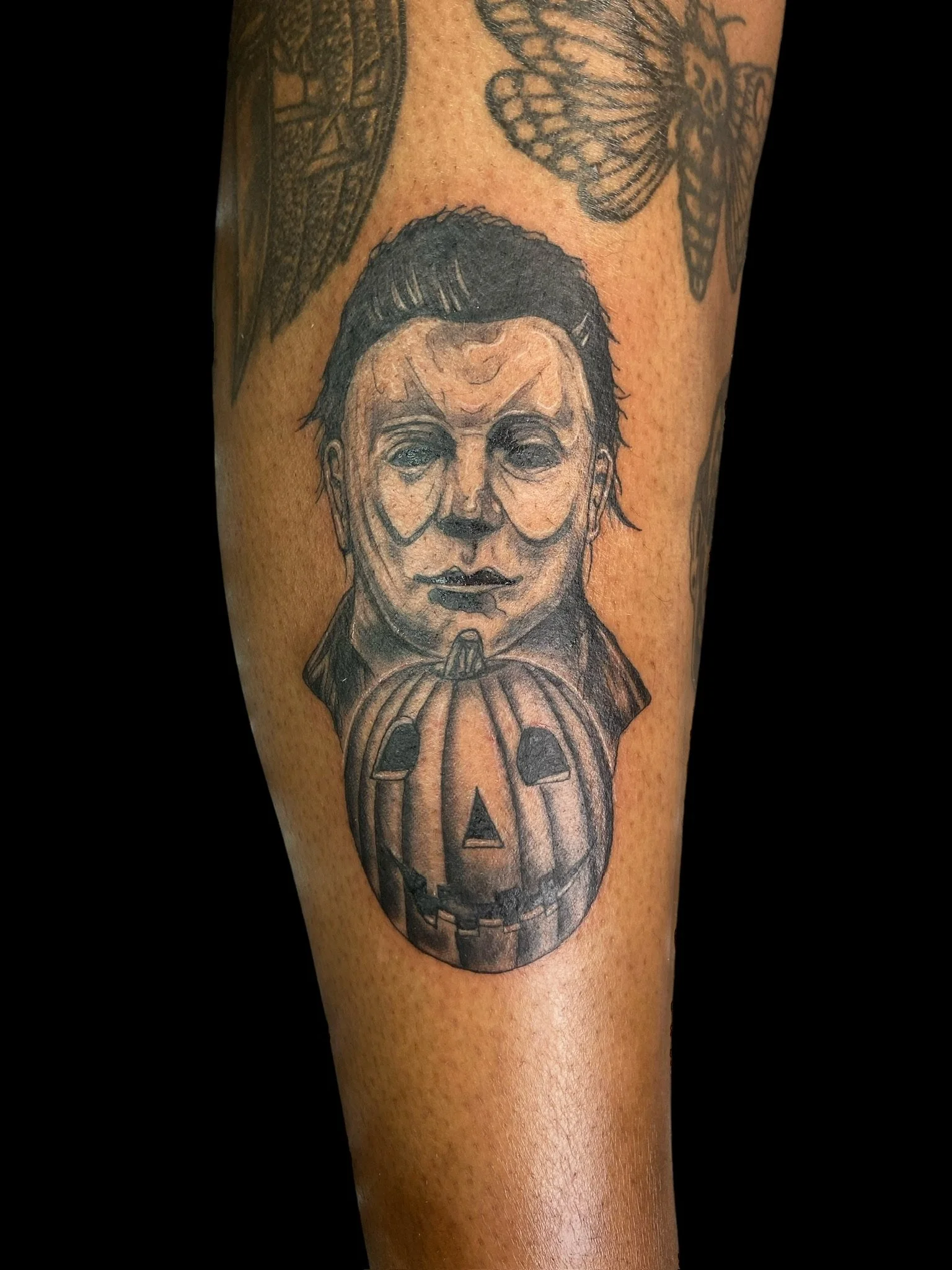 A tattoo of a person with short hair, a stern expression, and hands pressed together below their chin, with a large pumpkin underneath.