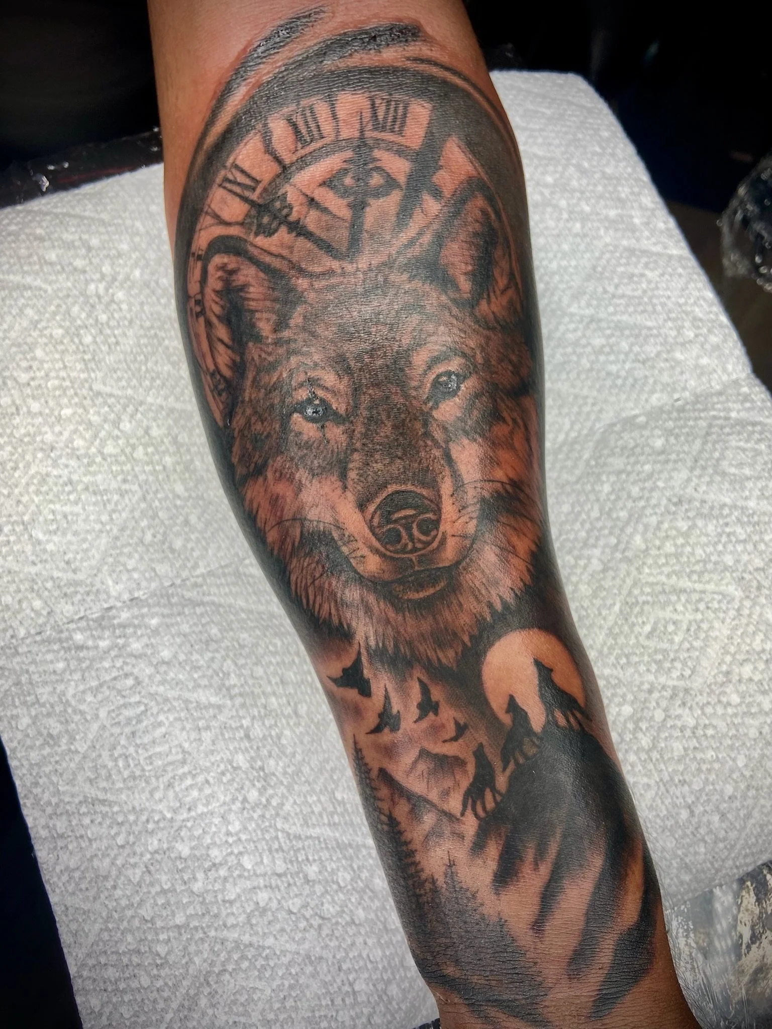Tattoo of a wolf's face with a clock above its head, and a moon and silhouettes of bats underneath.