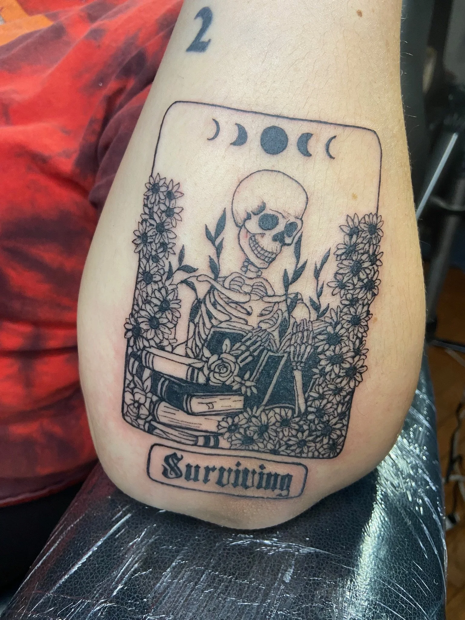 Tattoo of a human skeleton surrounded by flowers, with moon phases above and the word 'Sruyng' written below.