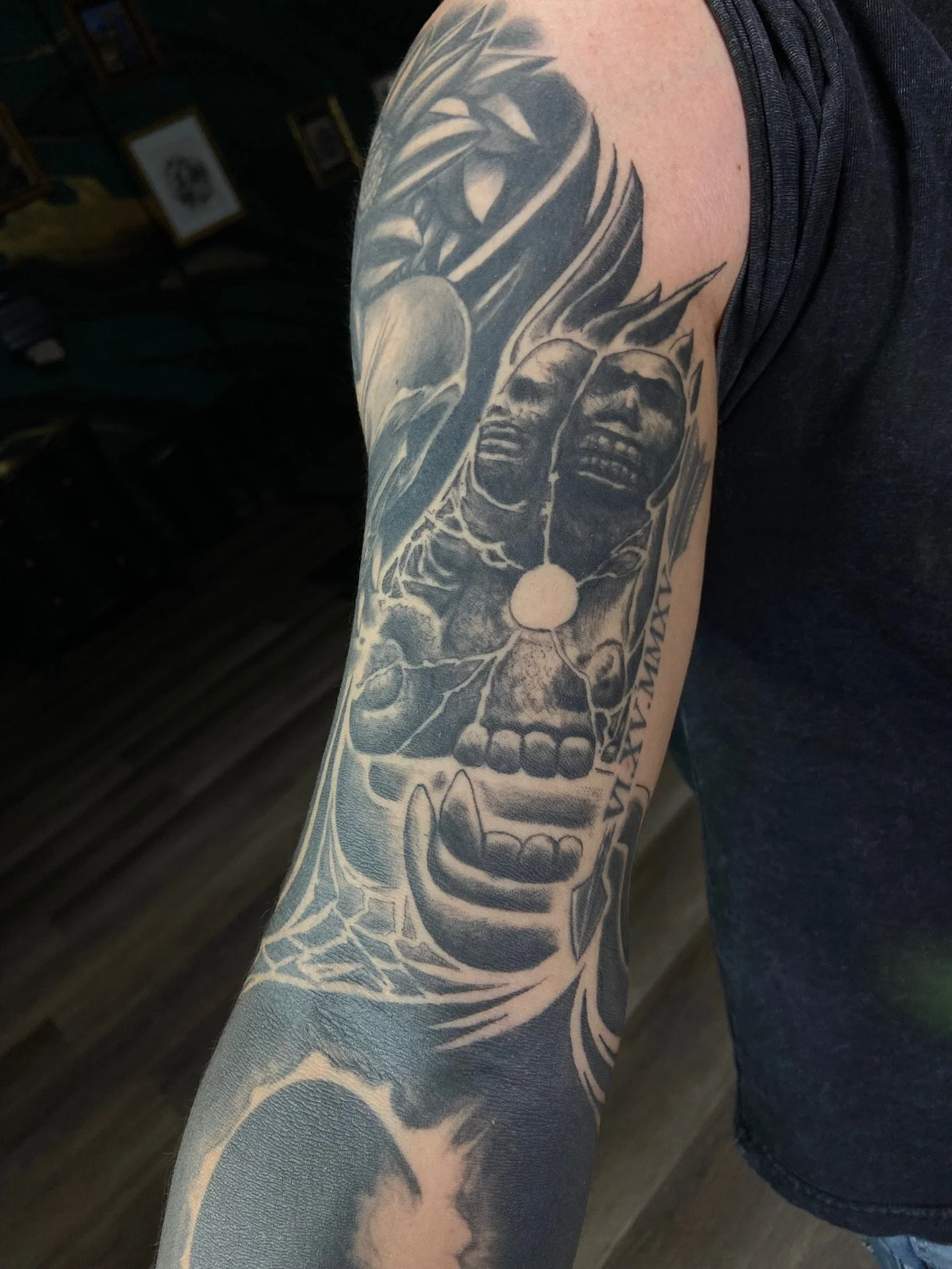 A tattoo on a person's arm featuring a skull, flowers, and abstract elements in black and gray ink.
