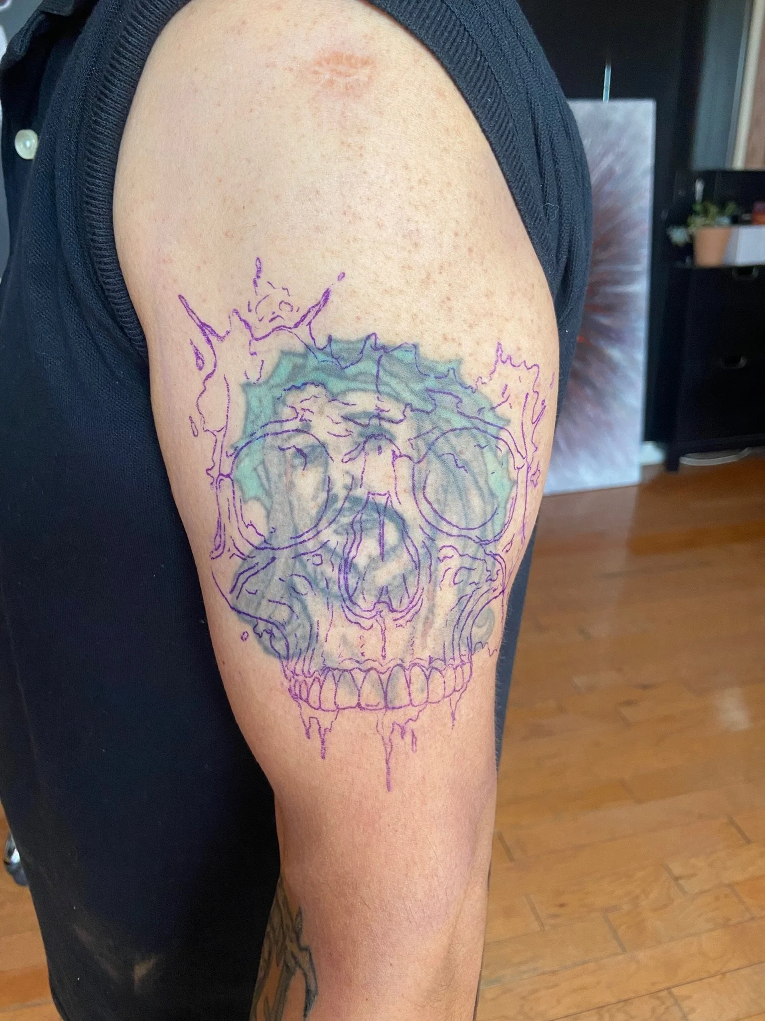 A person with a tattoo outline of a human skull on their upper arm. The tattoo is drawn with purple ink and appears to be a temporary outline.