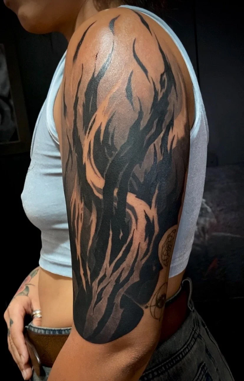Tattoo of a tree with bare, twisted branches on a person's upper arm. Blackwork full shoulder sleeve tattoo.