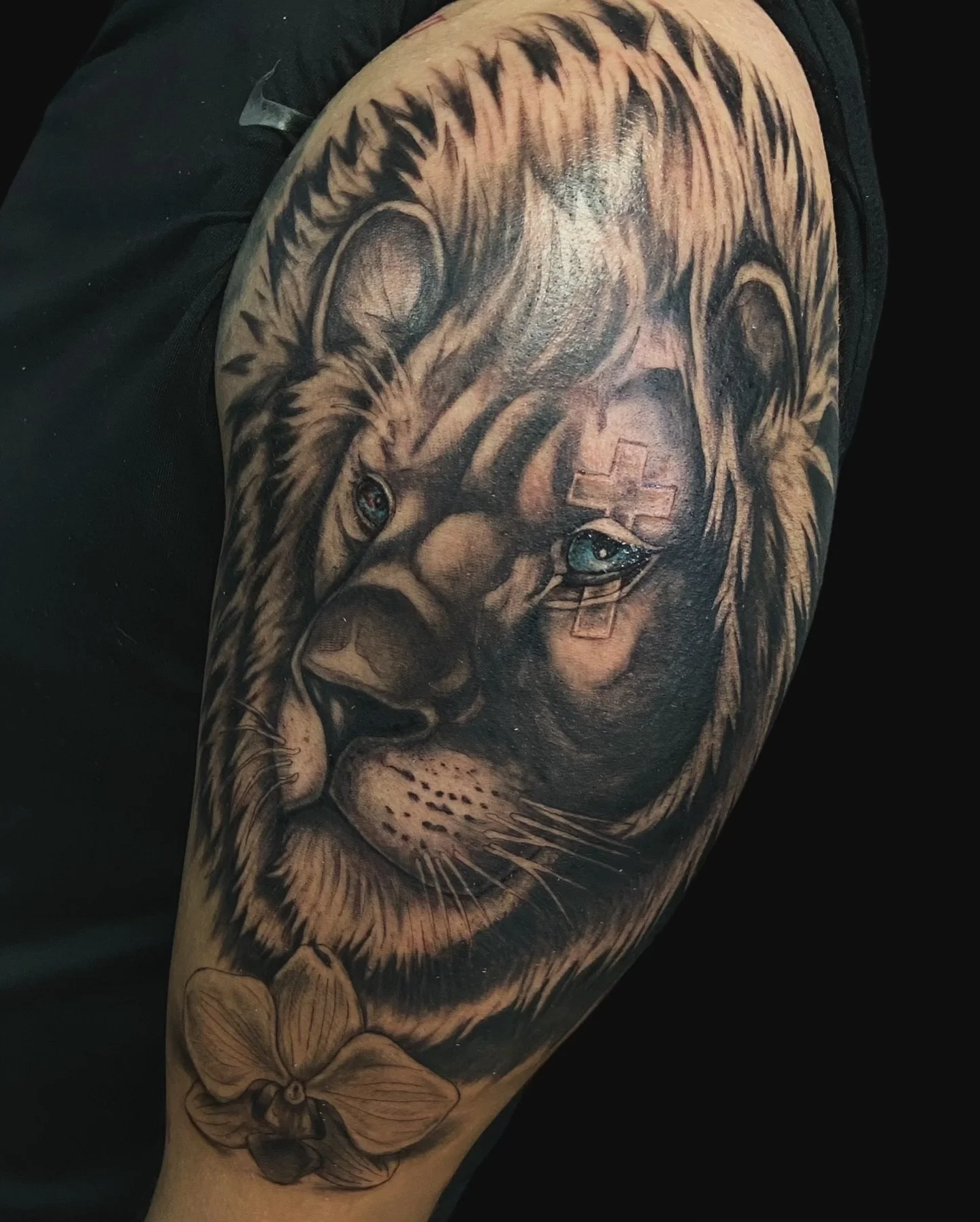 Tattoo of a lion's face with detailed fur, piercing eyes, and a medical cross on its forehead, on a person's arm.