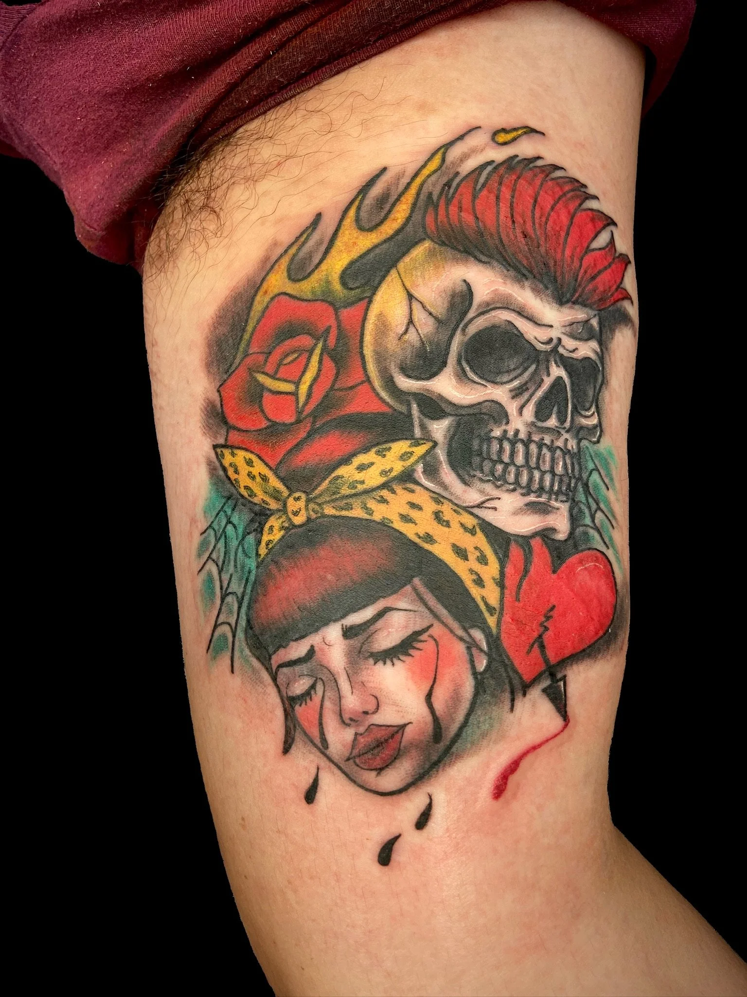 Tattoo of a woman's face with closed eyes, red lipstick, and a headscarf, combined with a skull with red hair, flames, a red rose, and a yellow bandana.