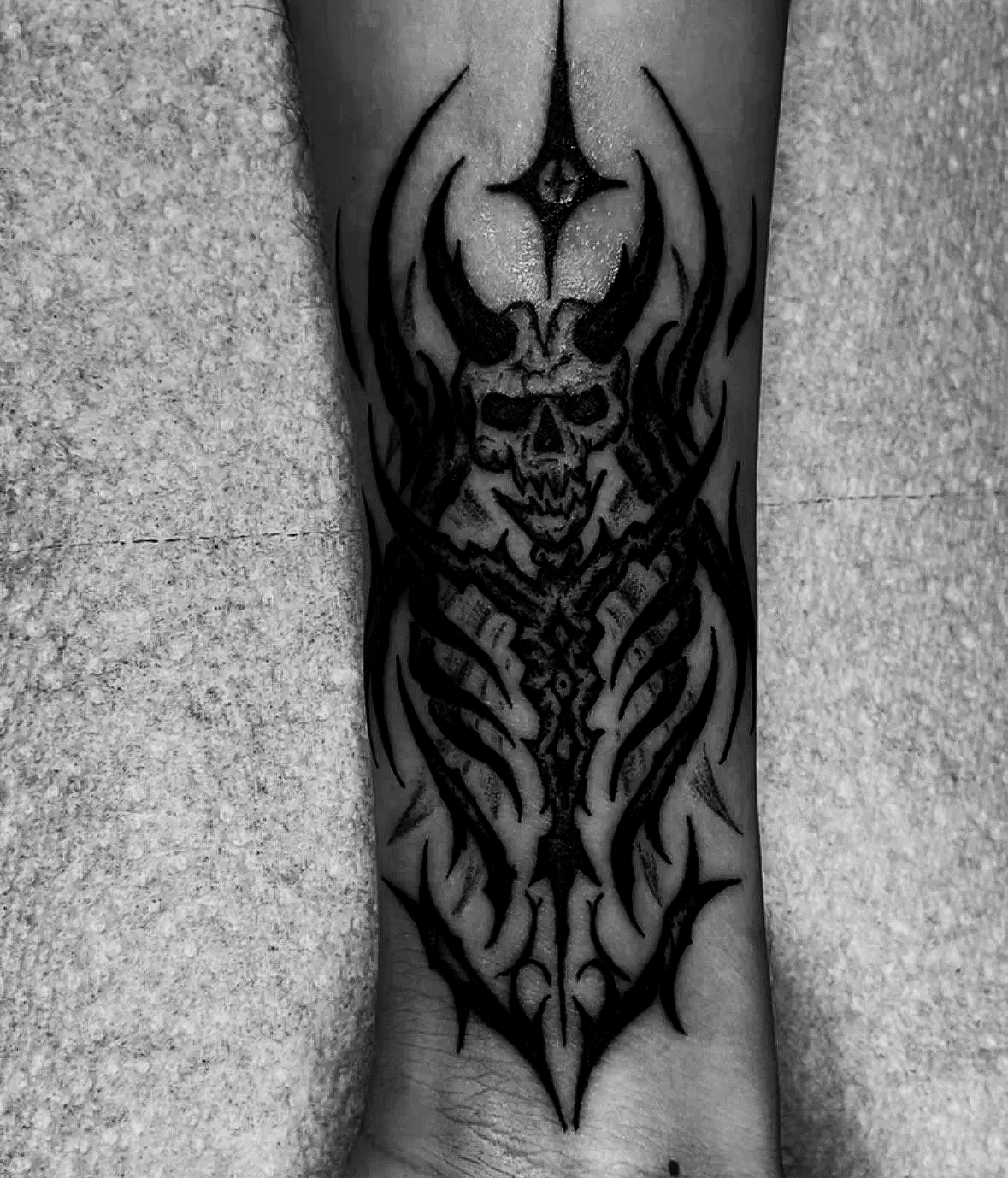 Black and gray tattoo on a person's forearm featuring a skull with flames and tribal elements.