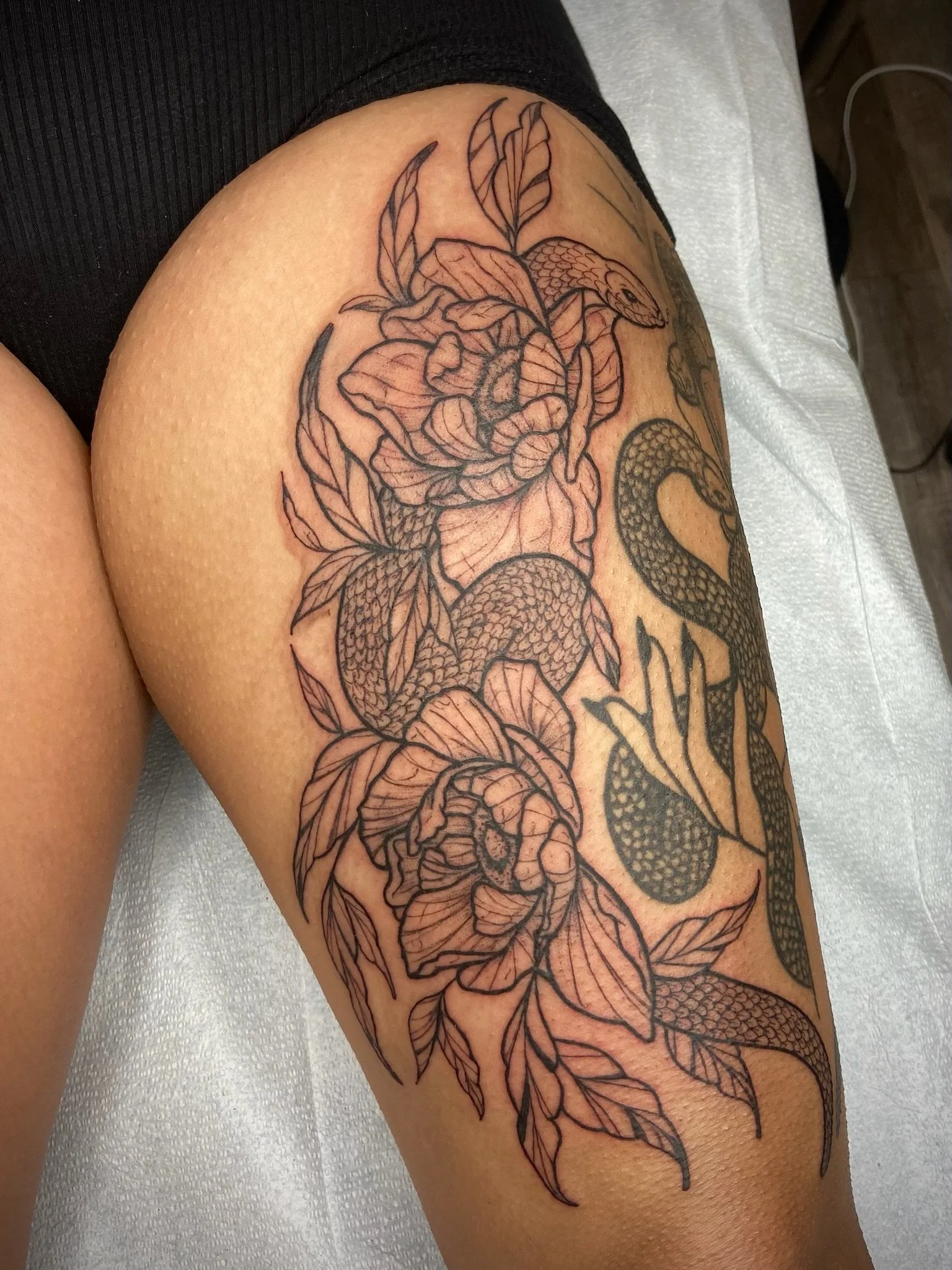 Black outline tattoo of a snake and flowers on a person's upper arm.