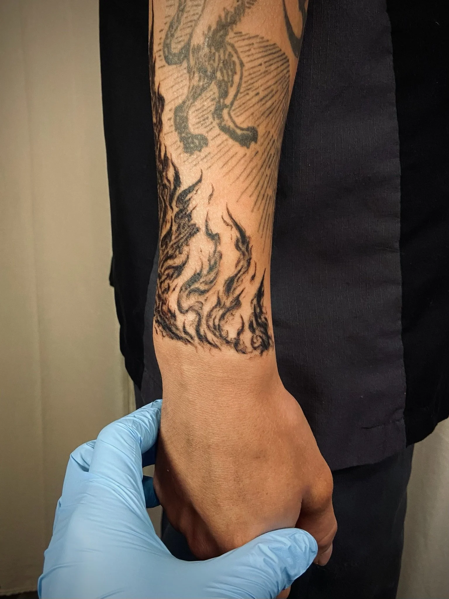 A person with a sleeve tattoo on their arm is having a tattoo done by a tattoo artist wearing blue gloves.