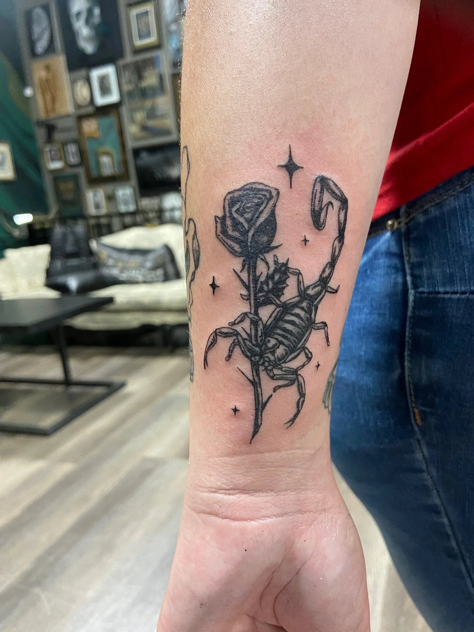 Tattoo of a scorpion holding a rose on a person's inner forearm, with stars around the design.