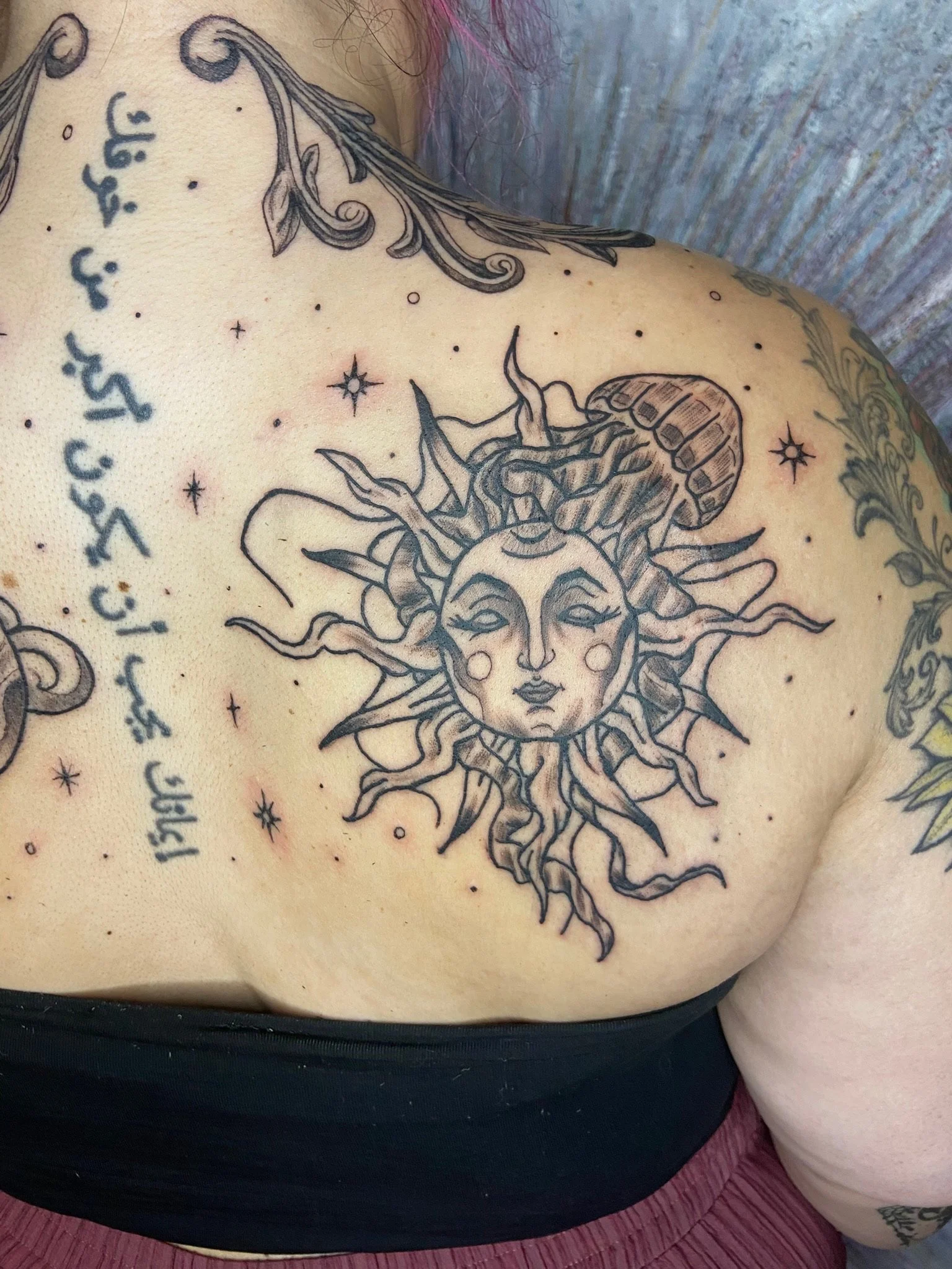 Tattoo of the sun with a woman's face, surrounded by stars, on a person's chest.