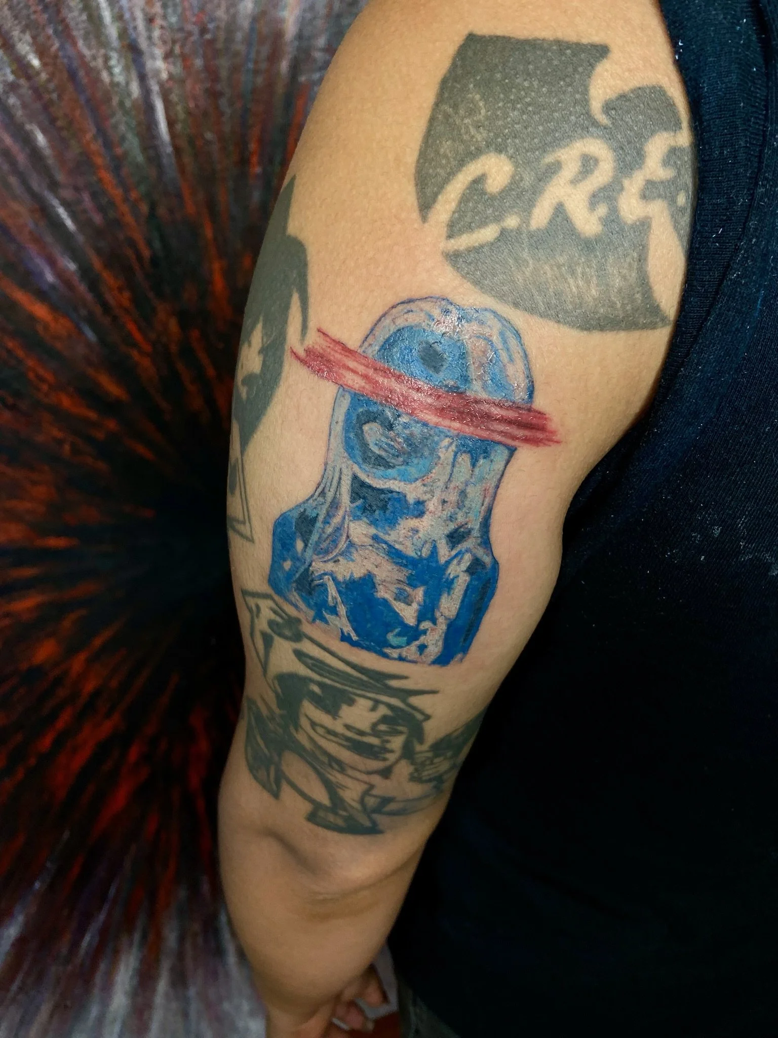 Tattoo on person's upper arm featuring a dark emblem with the word 'CRIME', an illustration of a human brain with a red slash through it, and abstract black and gray designs.