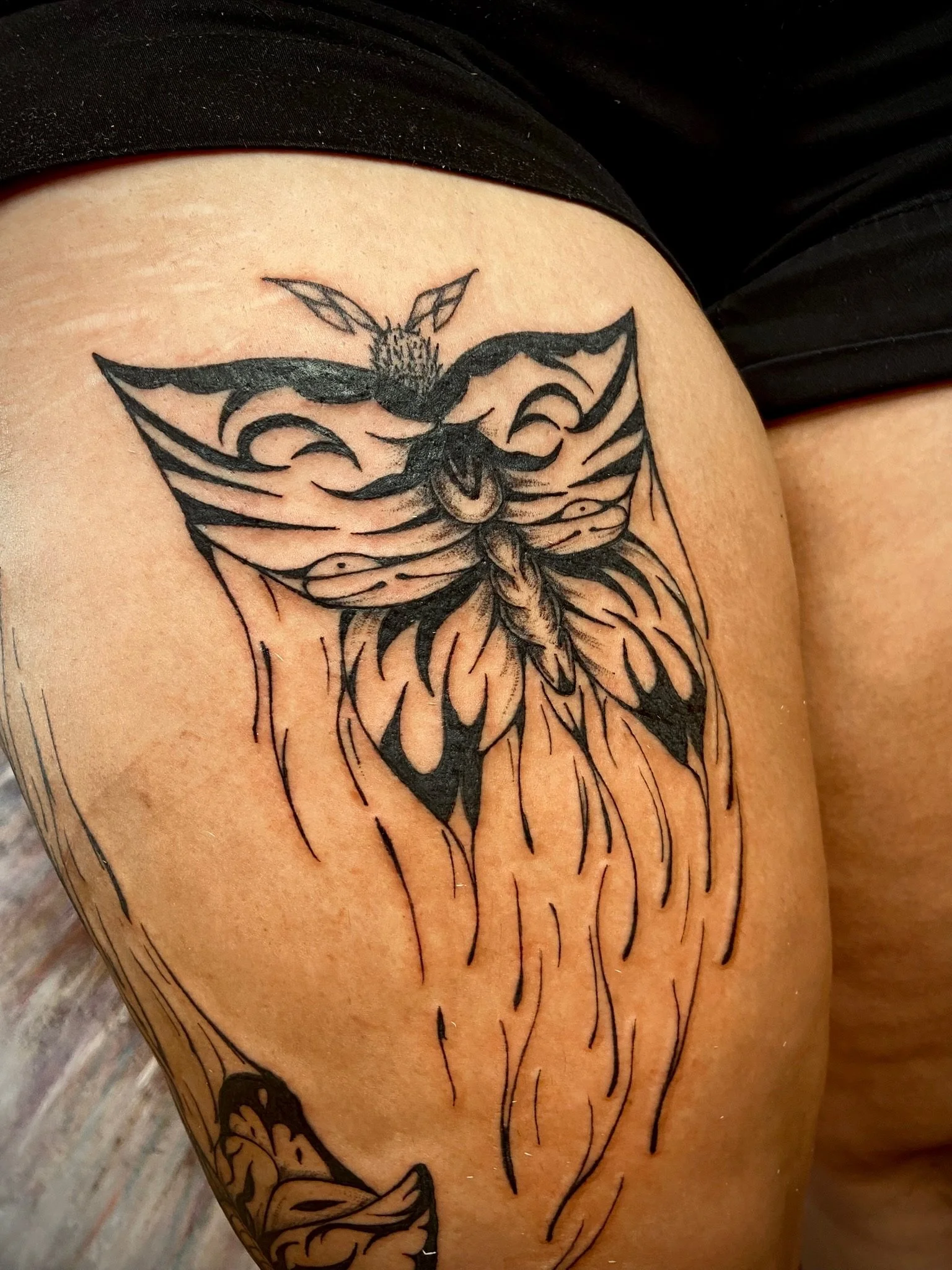 A black ink tattoo of a butterfly with open wings on a person's upper arm.