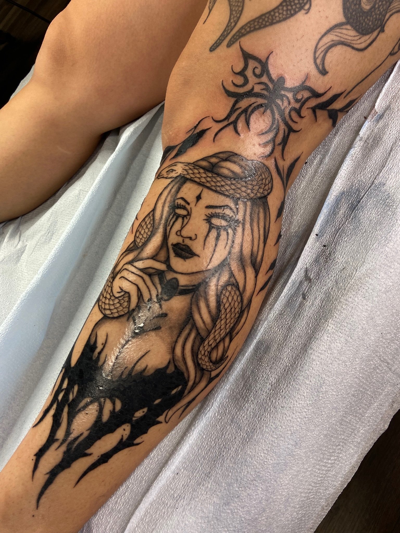 A tattoo sleeve featuring a woman with long hair, a snake wrapped around her head, and various tribal and animal designs.