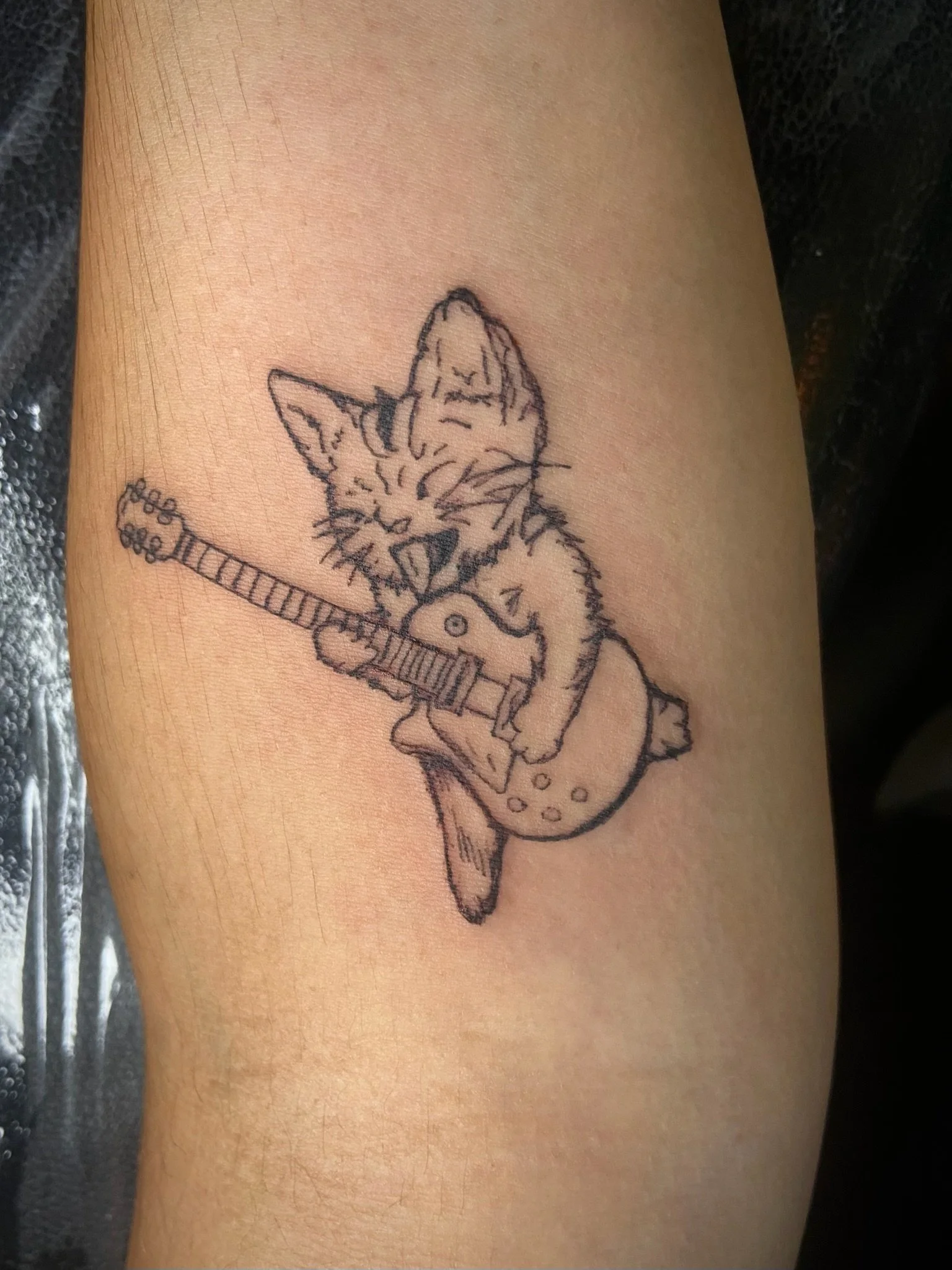 Tattoo of a grumpy cat playing an electric guitar on a person's skin.