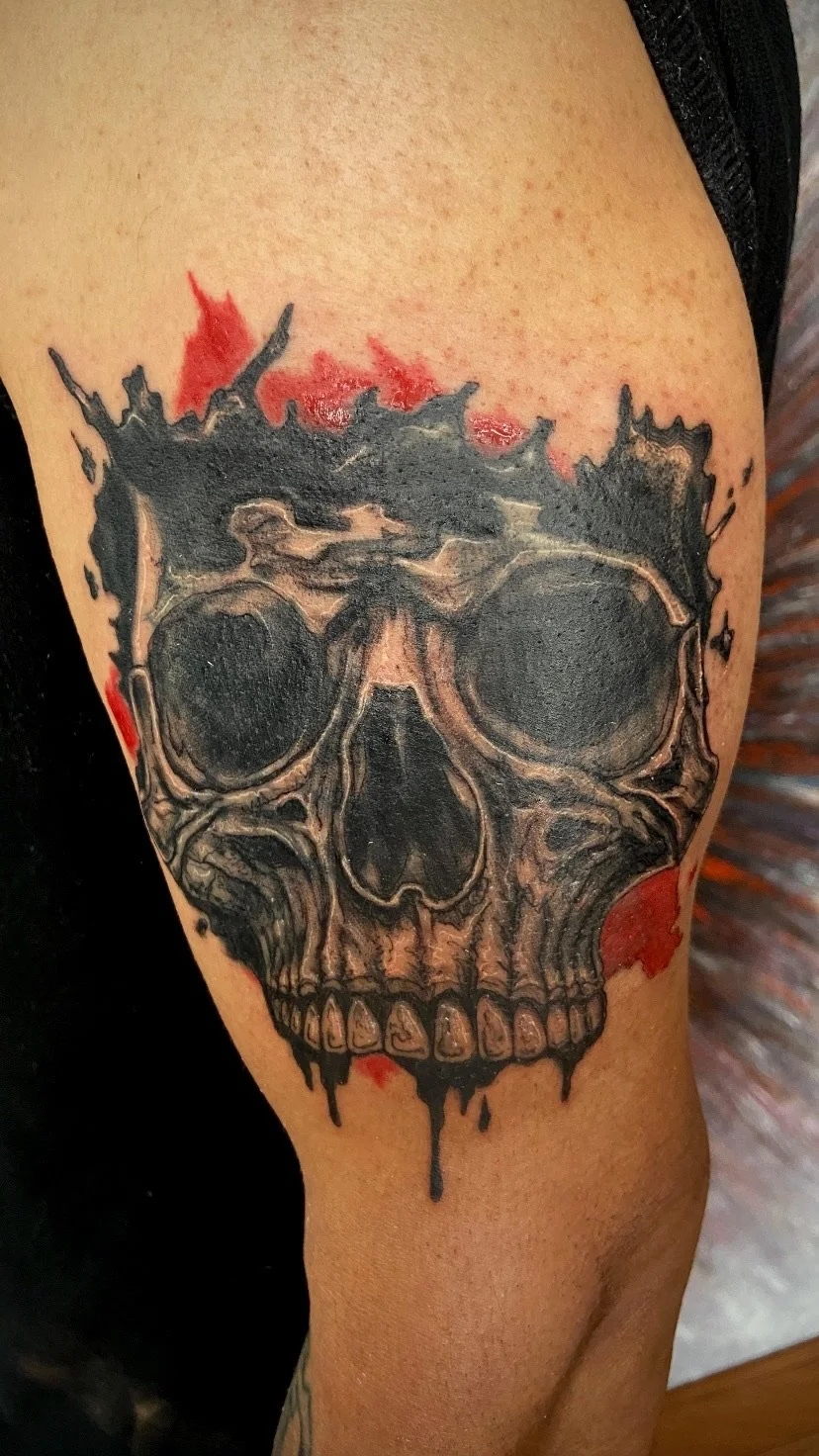 A tattoo of a realistic skull on a person's upper arm, with red and black ink accents around it.
