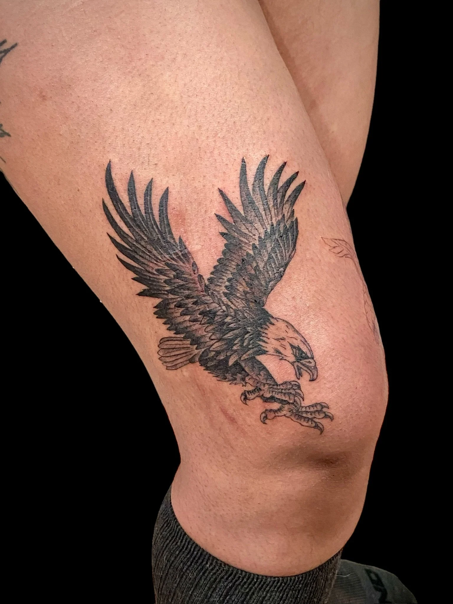 Tattoo of a detailed black eagle with wings spread, perched on a person's upper arm.