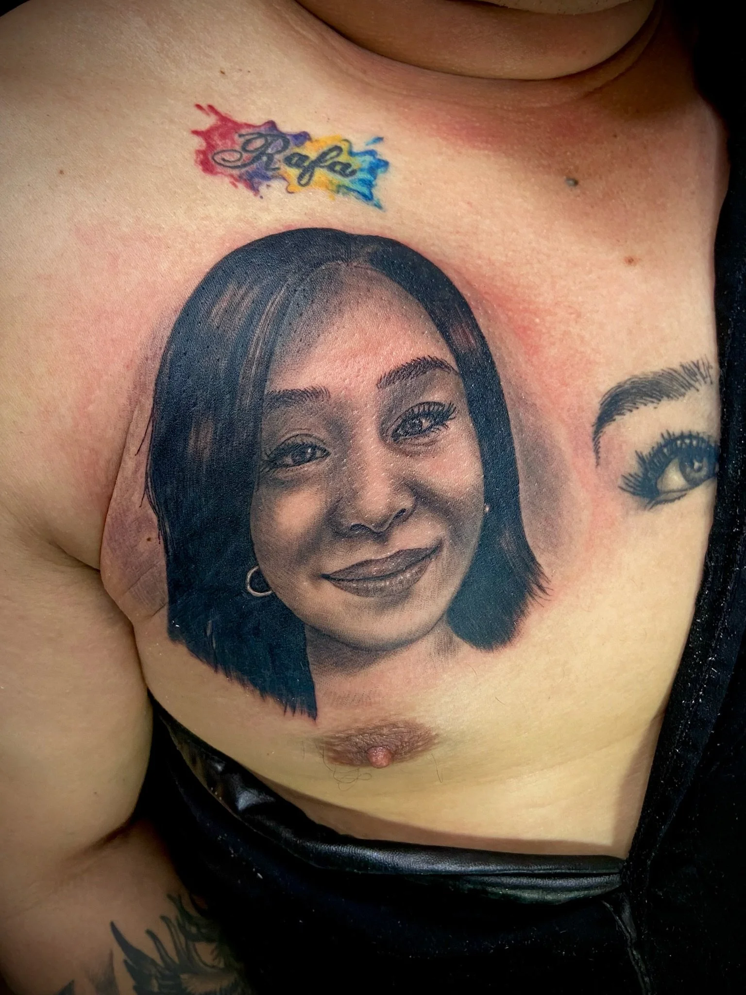 Tattoo of a woman's face on a person's chest with tattooed text above it that says "Rafa" in colorful script.