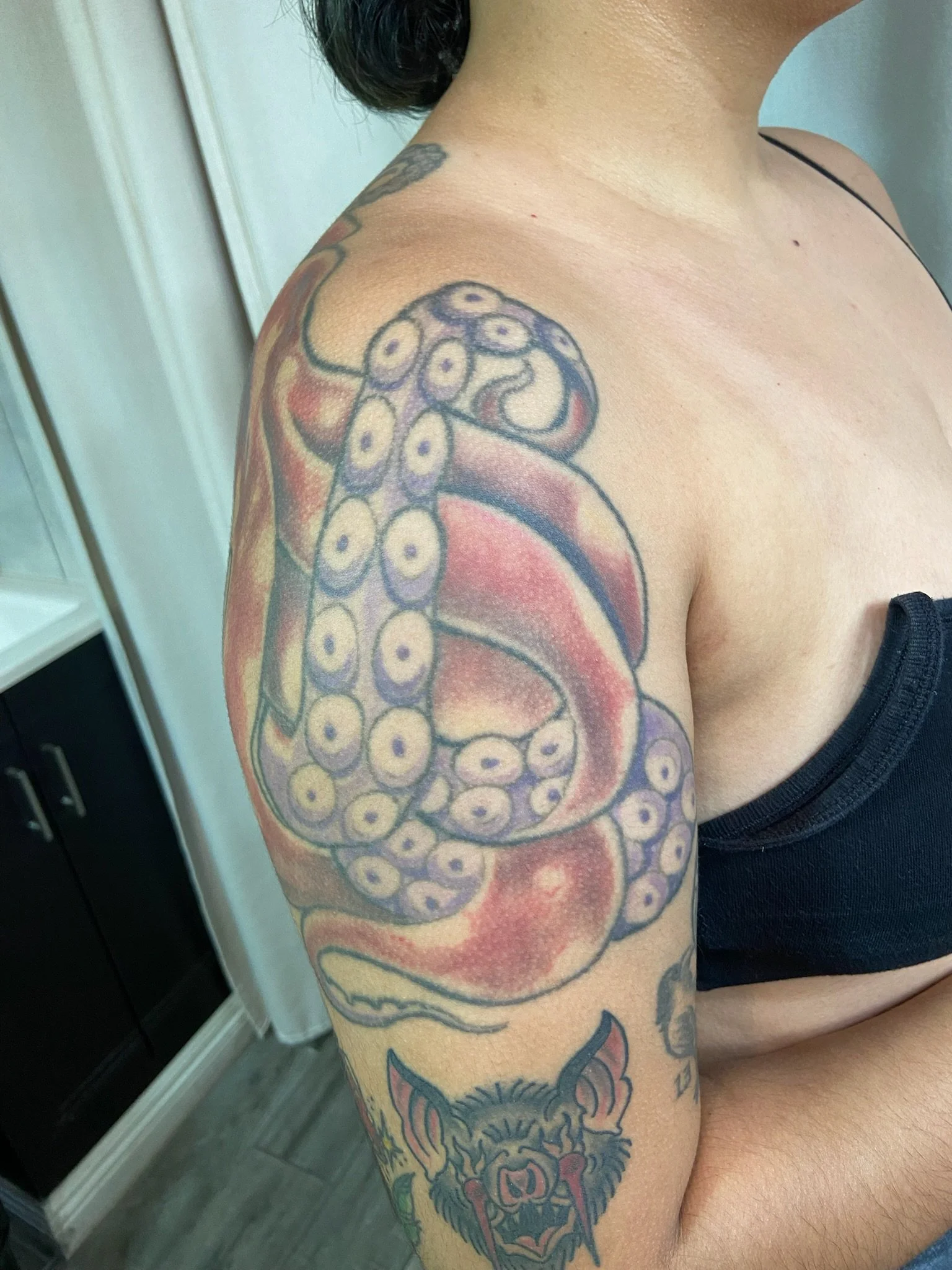 A person's upper arm and shoulder with a colorful tattoo of an octopus, with detailed eye and tentacle designs.