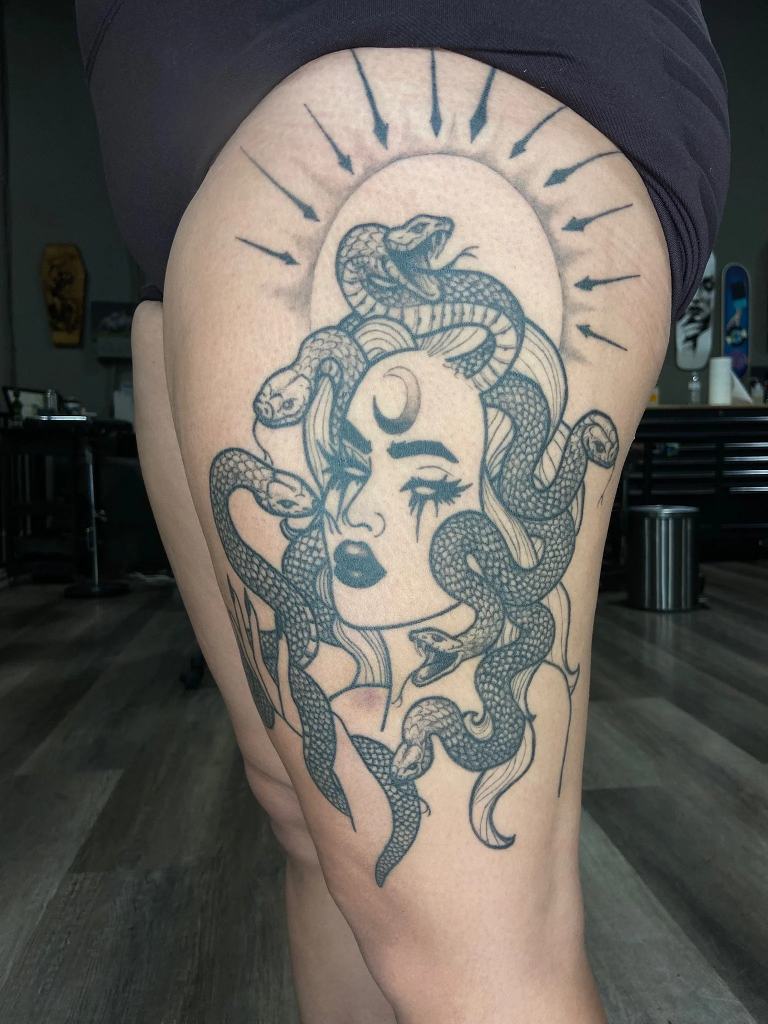 A tattoo of a snake wrapped around a woman's face with a crescent moon and radiating lines around the head.