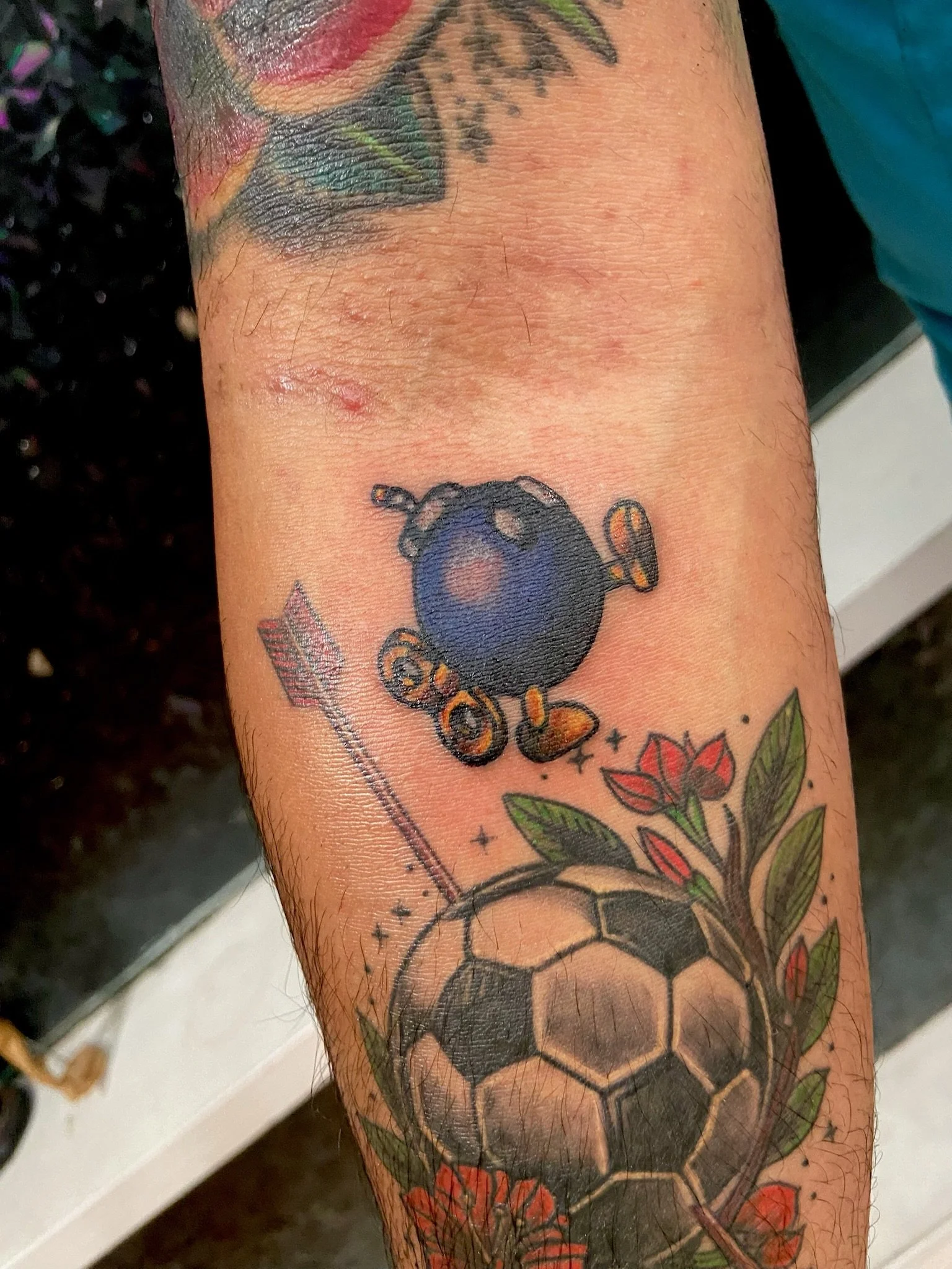 Close-up of a tattoo on a person's forearm, featuring a cartoonish bomb with a lit fuse, surrounded by colorful flowers and a honeycomb pattern.