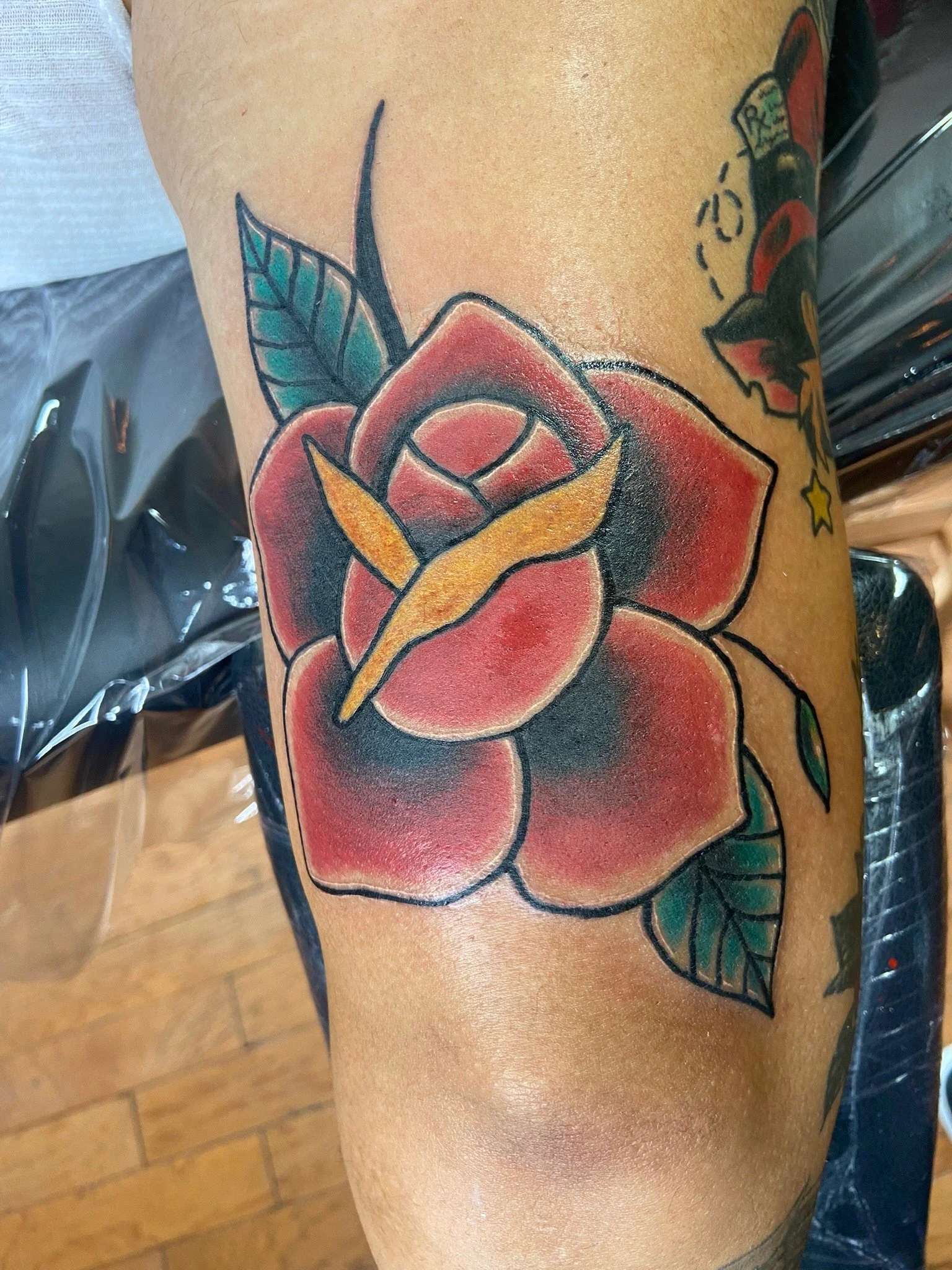 Colorful tattoo of a red rose with green leaves on a person's arm.