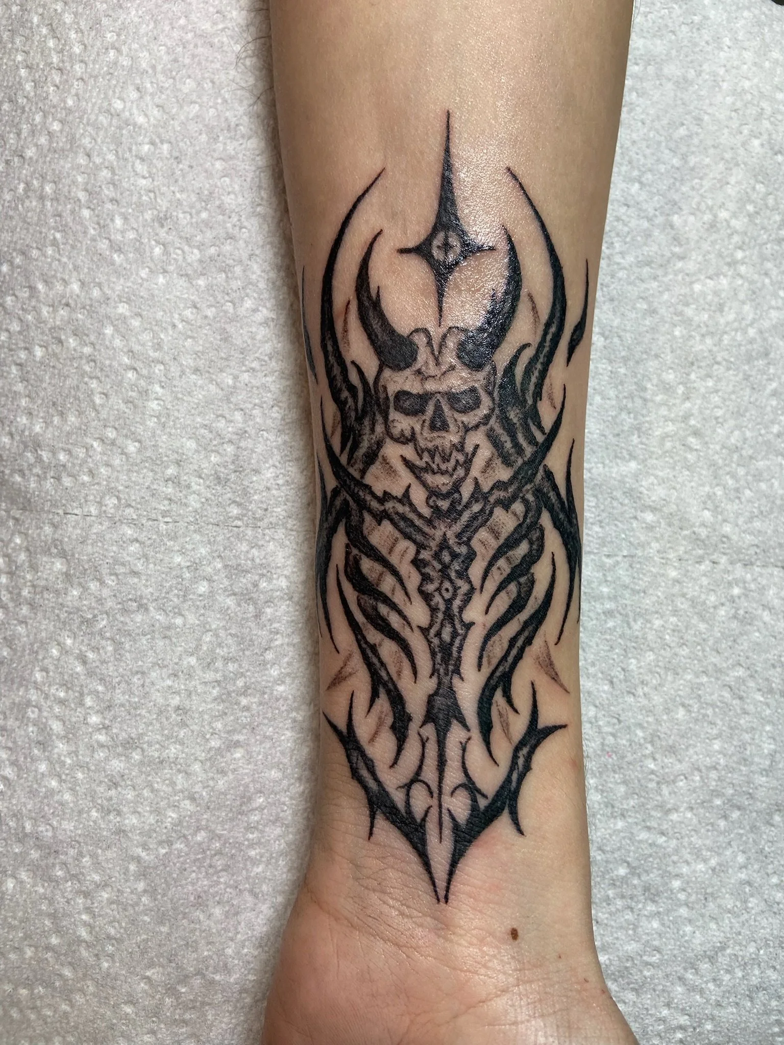 Tattoo of a knight's helmer with flames on a person's forearm. Blackwork tattoo and a hint of color.