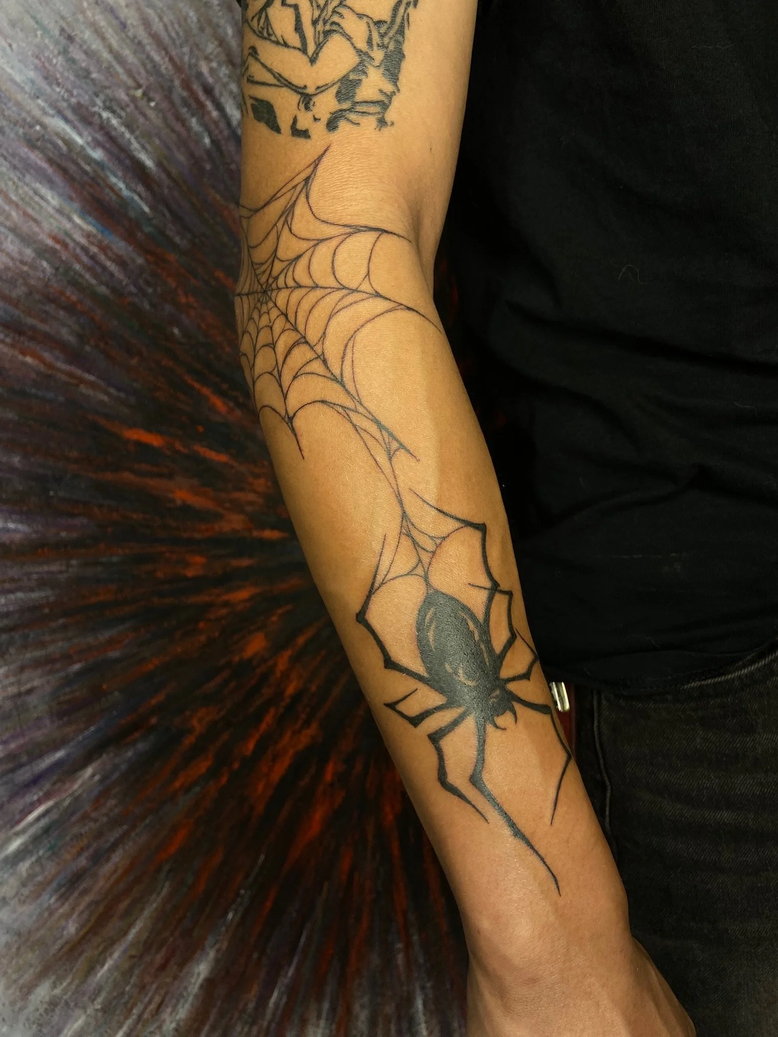 A person's forearm with a tattoo of a spider at the wrist and a spider web extending upwards.