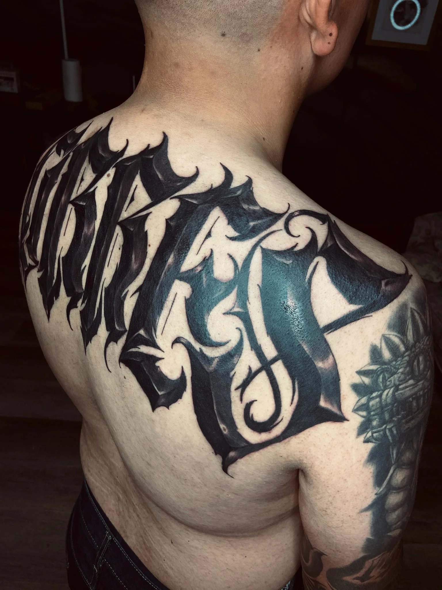 Close-up of a person's upper torso and shoulder with a large black tribal-style tattoo with sharp, angular shapes.
