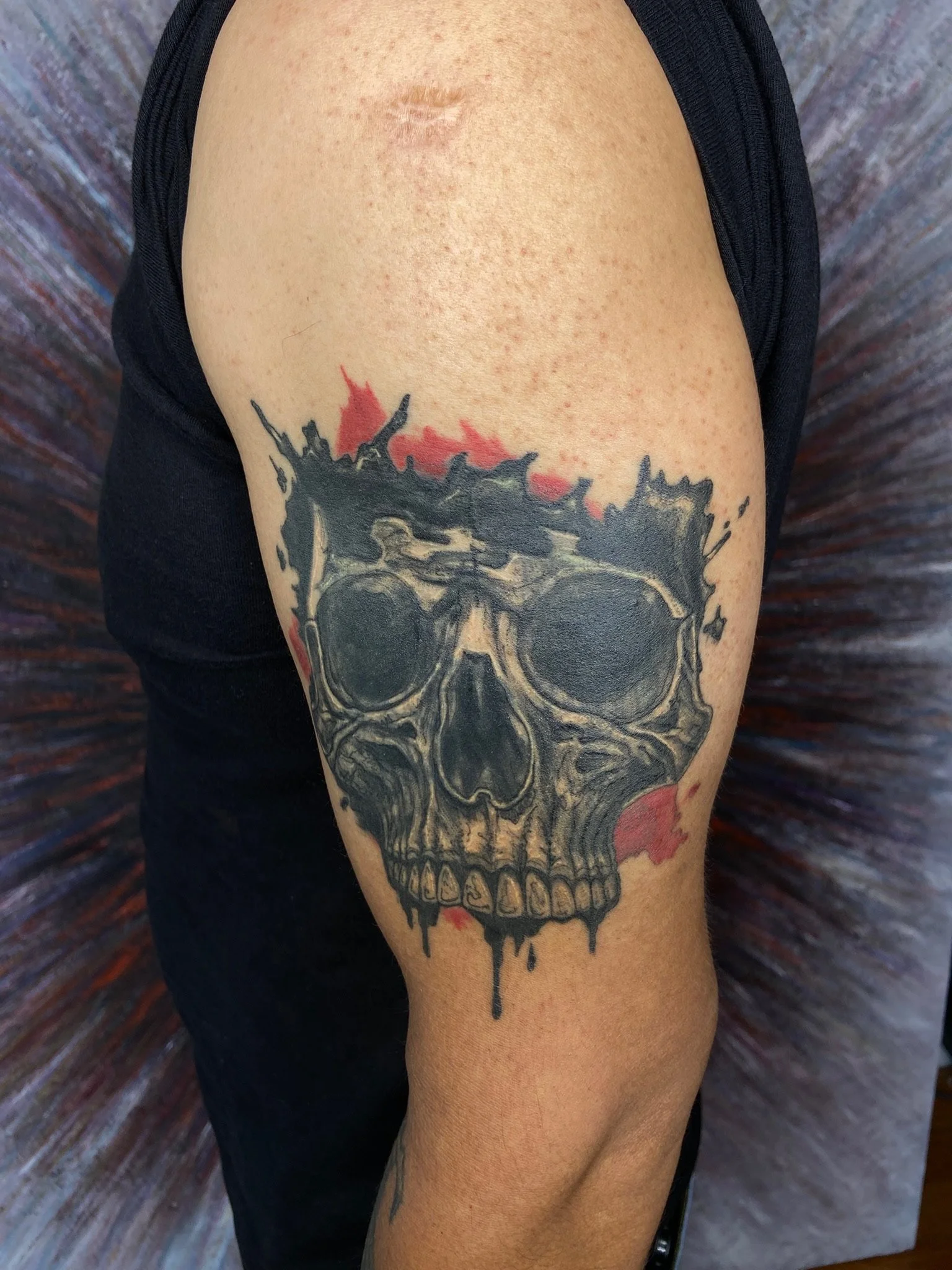 Tattoo of a skull with dripping paint effect on a person's upper arm.