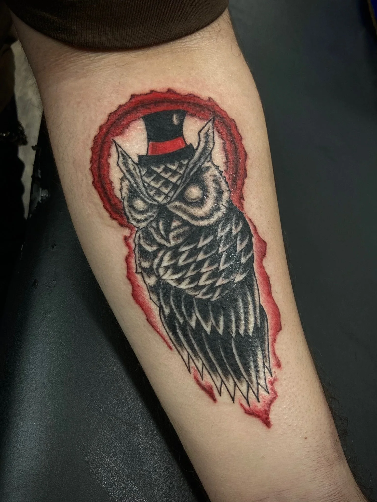 Tattoo of a grinning joker face wearing a top hat, with a red border around the design.