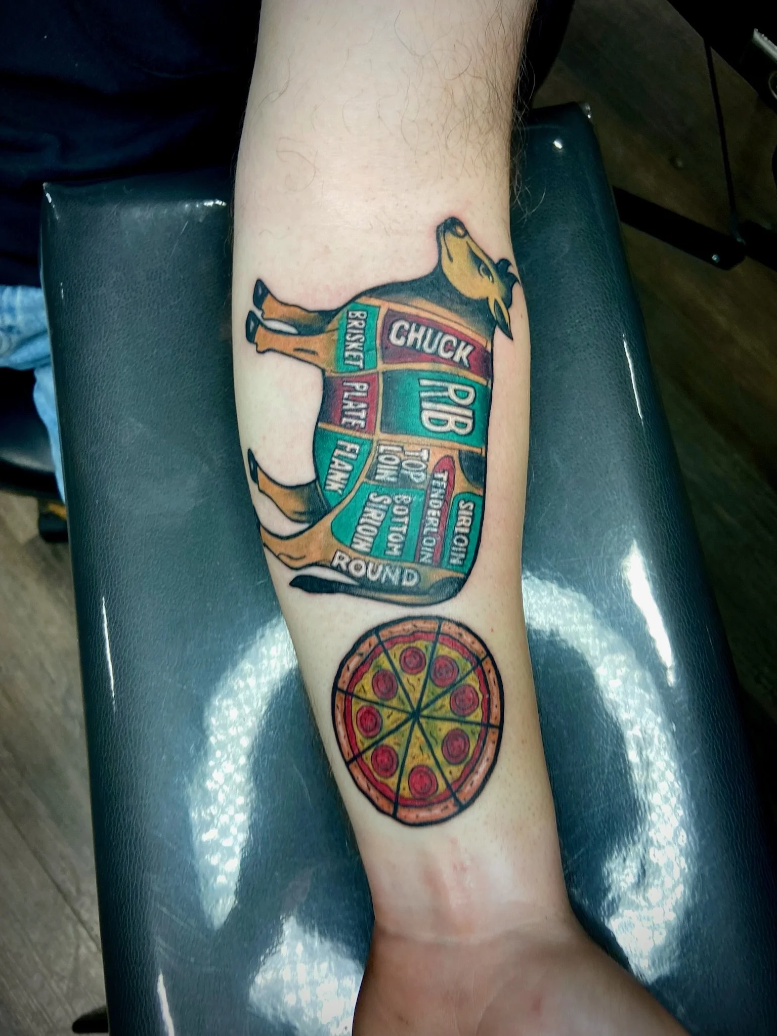 A tattoo of a pizza slice on a person's forearm, with colorful toppings and a golden crust.