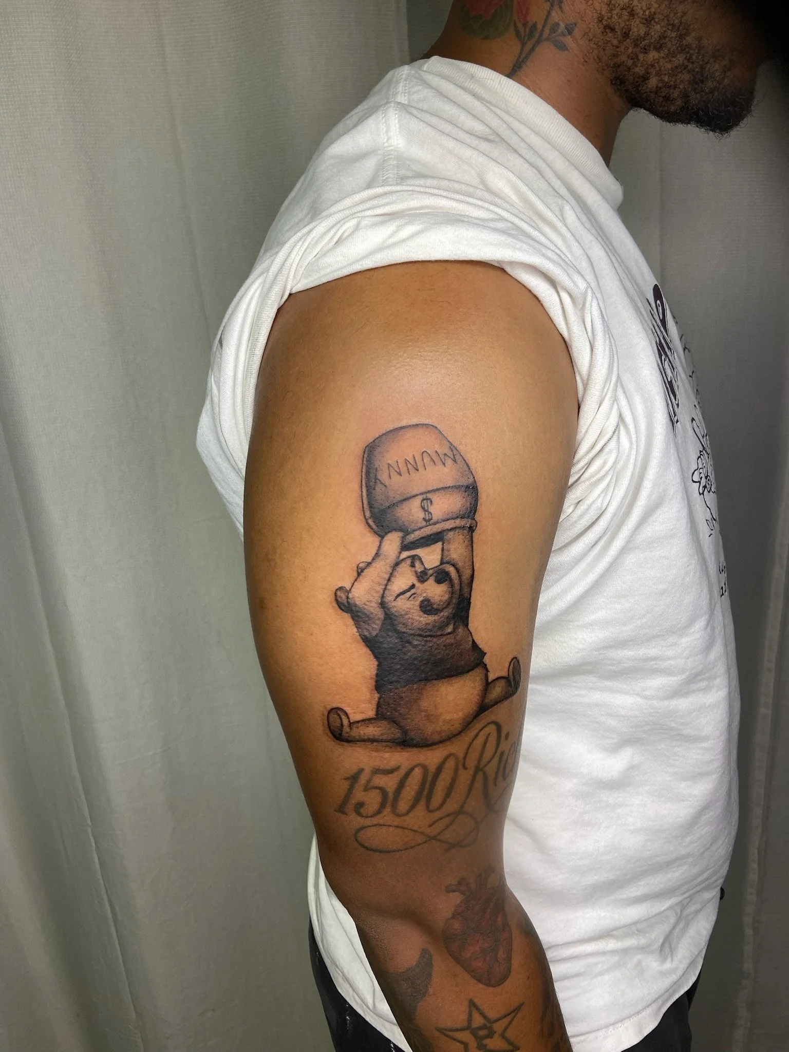 A person's upper arm with a tattoo of a cartoon character holding a balloon that says "MUNN" and a number "1500" written below.