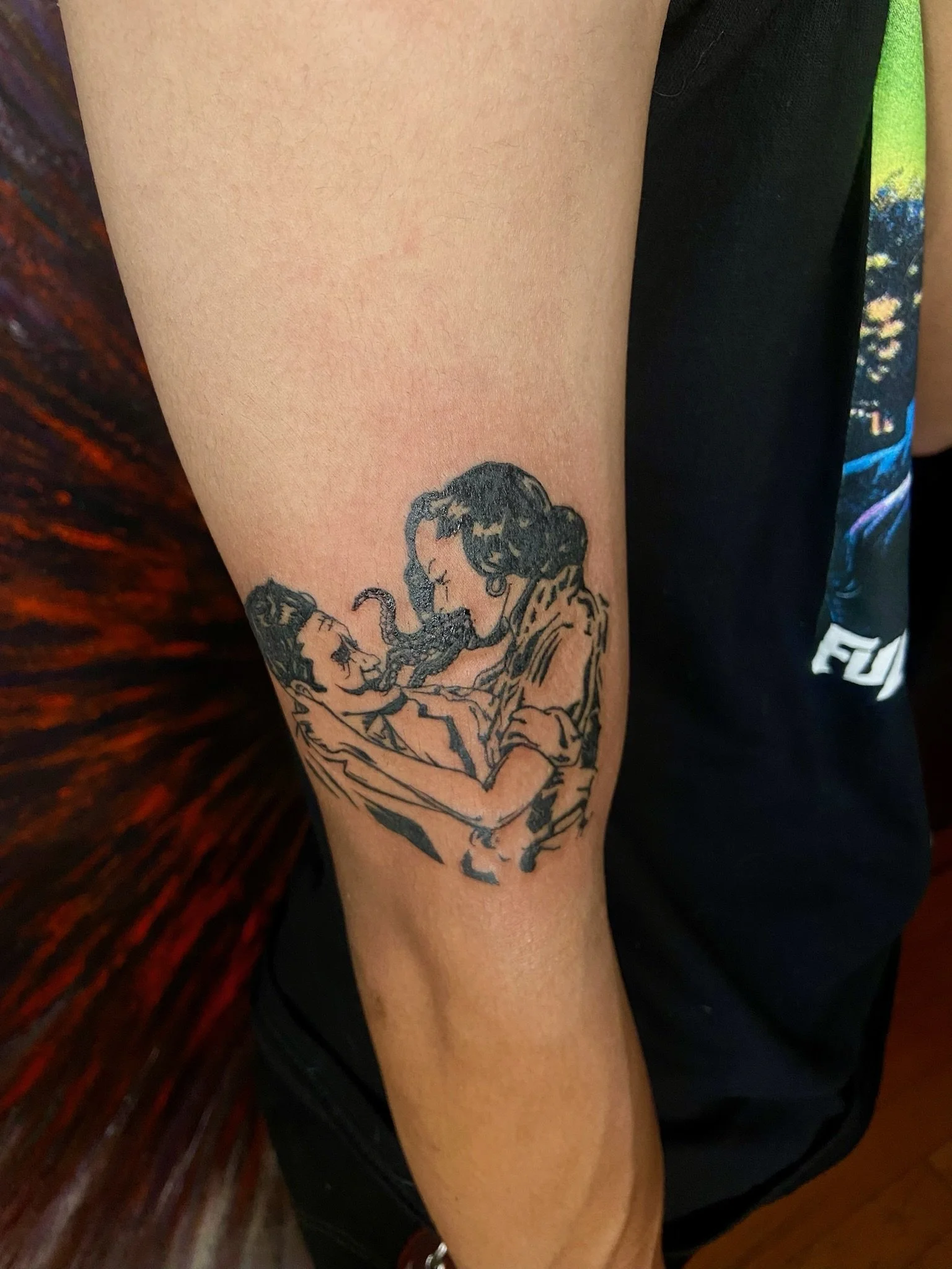 A tattoo of an old couple, a man and woman, facing each other and about to kiss, on a person's forearm.