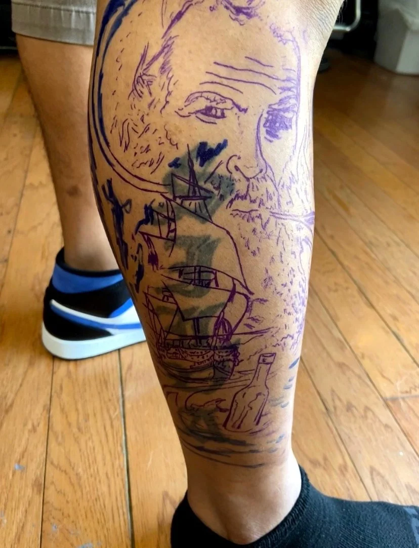 Tattoo of a bearded man's face with long hair, a ship on the sea, and a bottle on the ground, drawn with purple ink.