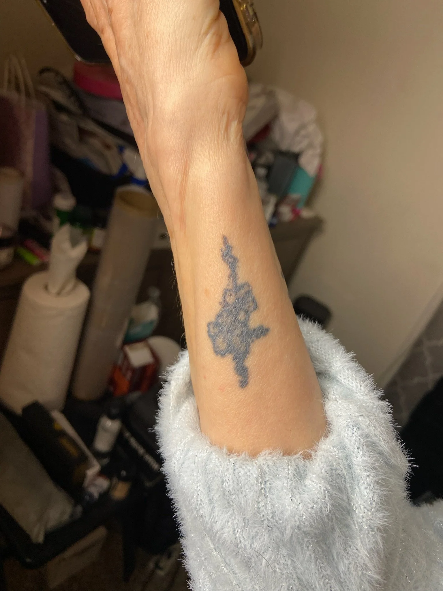 A person's arm with a star-shaped tattoo and a fuzzy white sleeve, held up in front of a cluttered background.