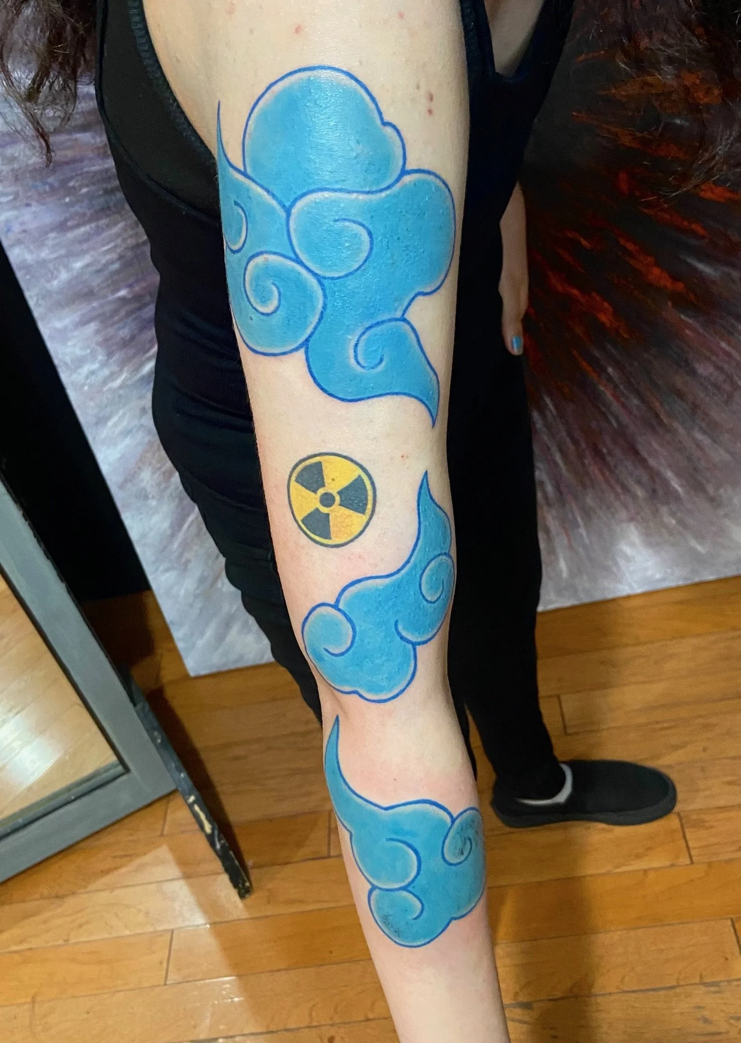 Tattoo of swirling blue clouds and a yellow radioactive symbol on a person's forearm.