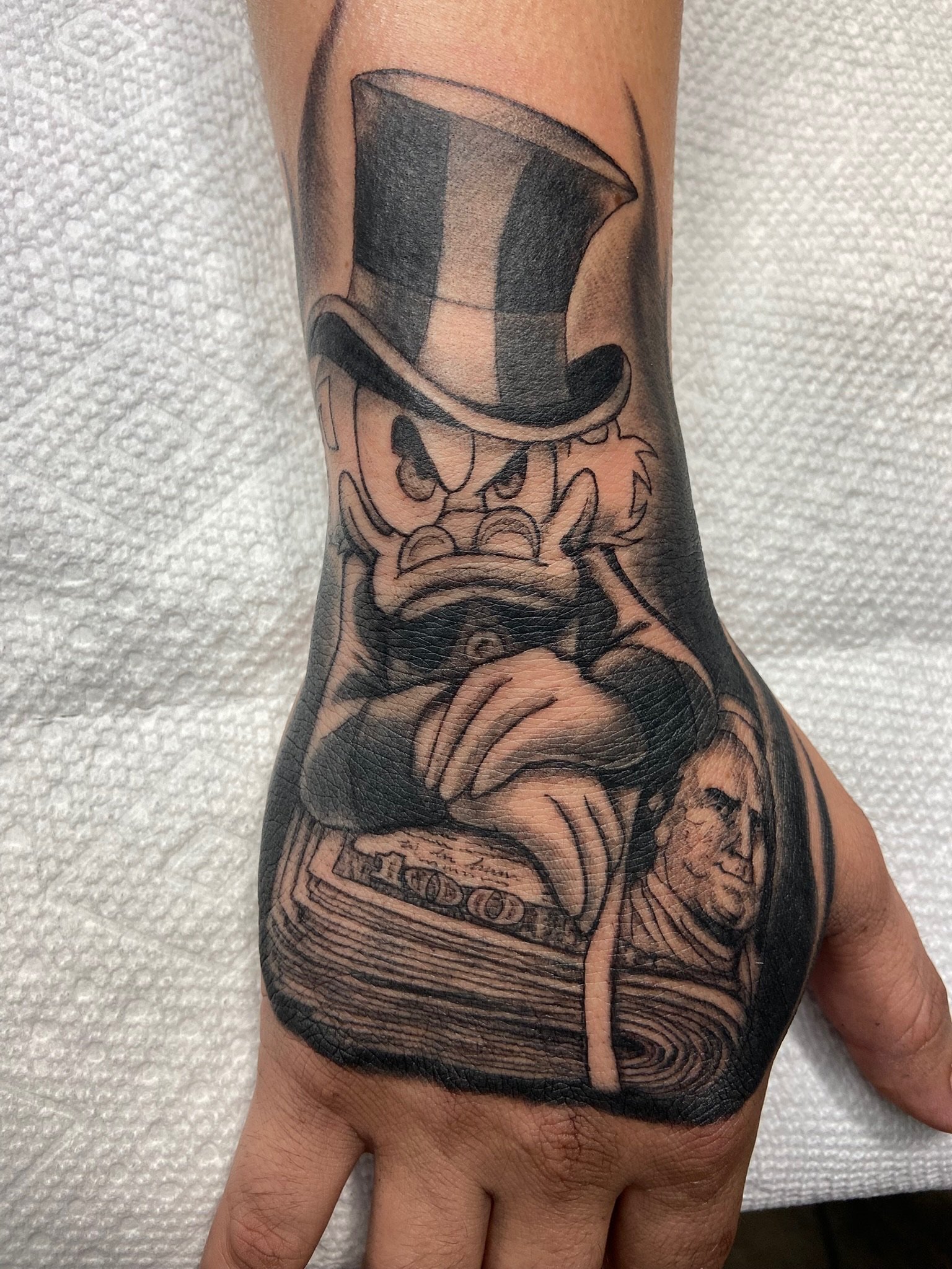 Tattoo of a top hat, a skull, a stack of money, and a woman's face on a person's arm.