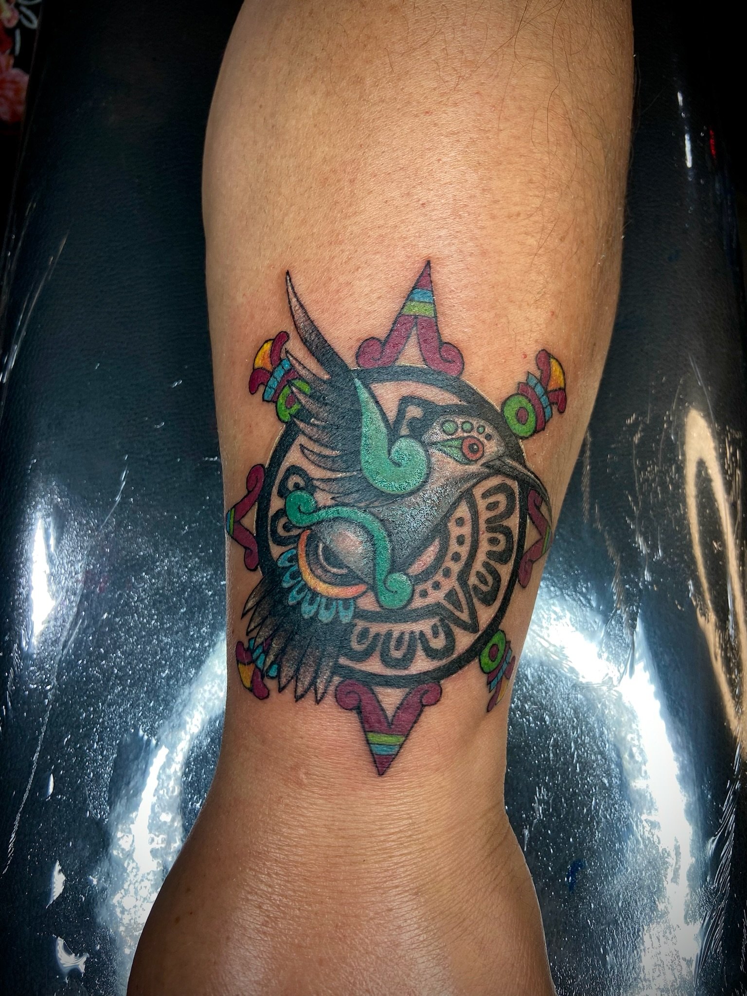 Colorful tattoo of a clock with wings, surrounded by decorative elements, on a person's leg.