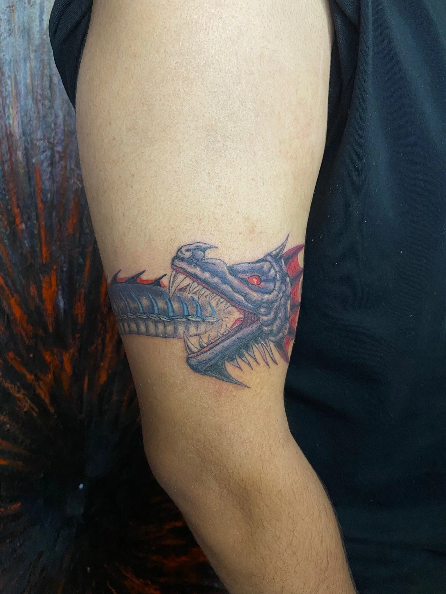 Tattoo of a dinosaur with open mouth on person's upper arm.