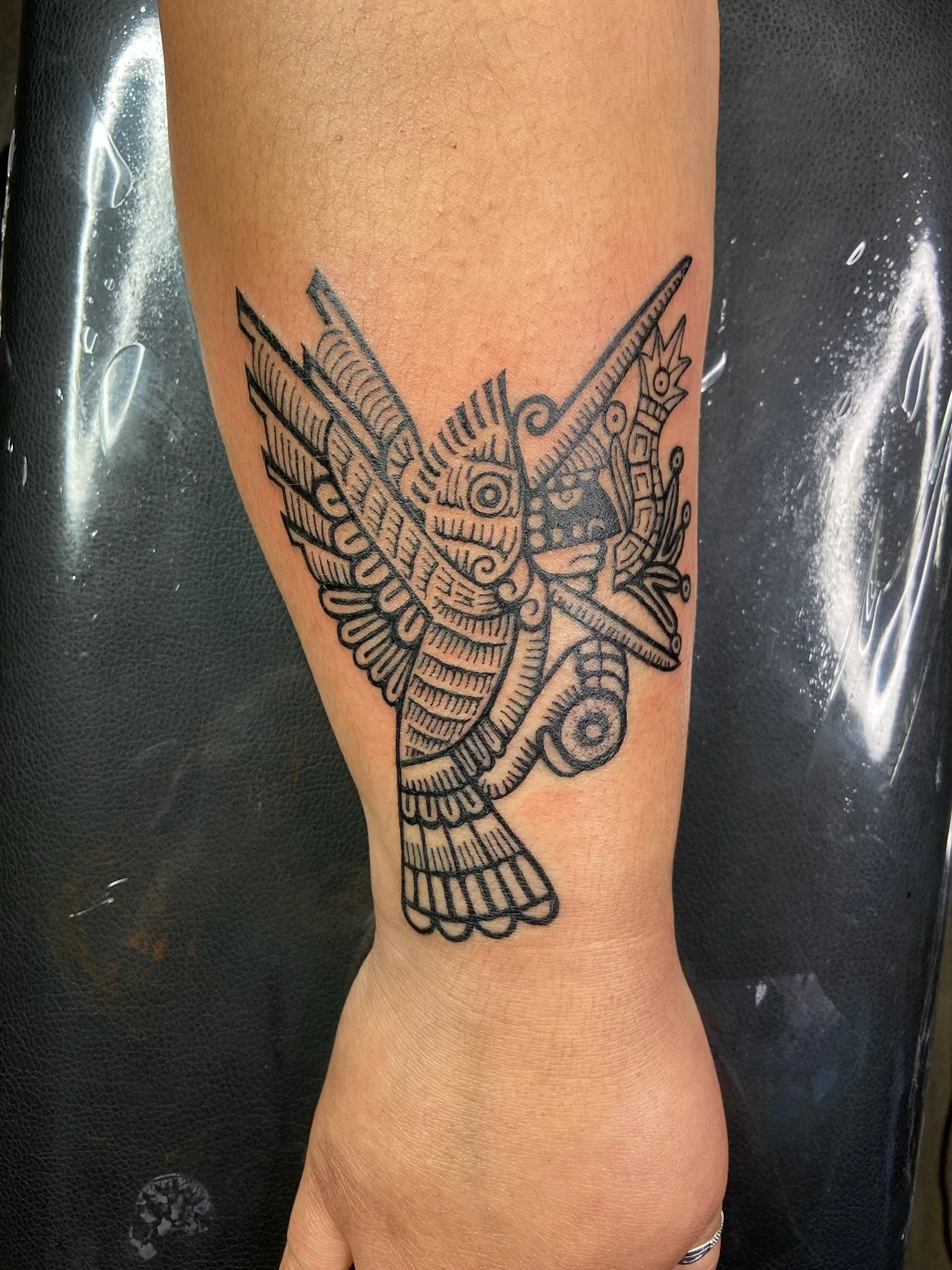 Black outline tattoo of a colorful symbolism on a person's upper arm.